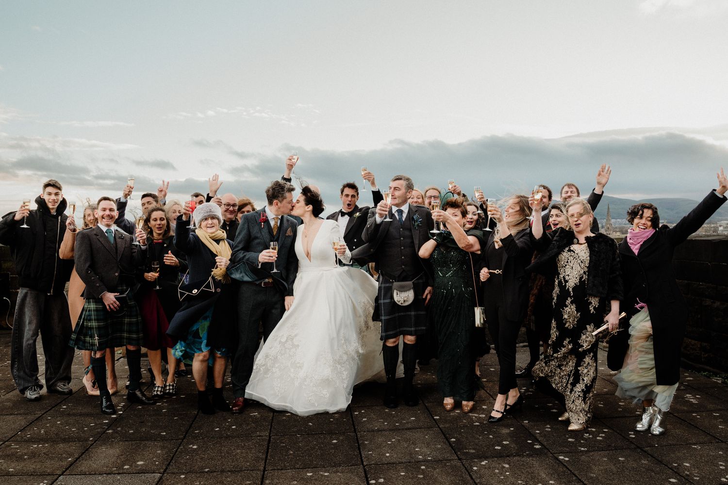 Wedding party in traditional Scottish kilts celebrates on castle grounds.
