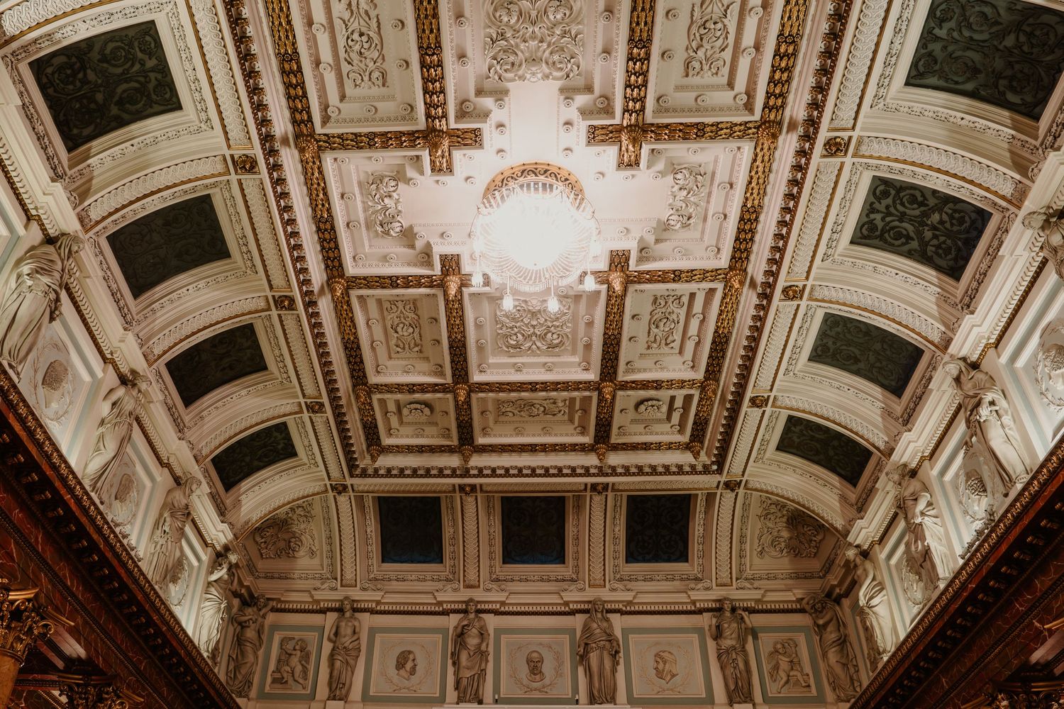 Ornate ceiling detail of a historic ballroom with intricate moldings and chandelier.