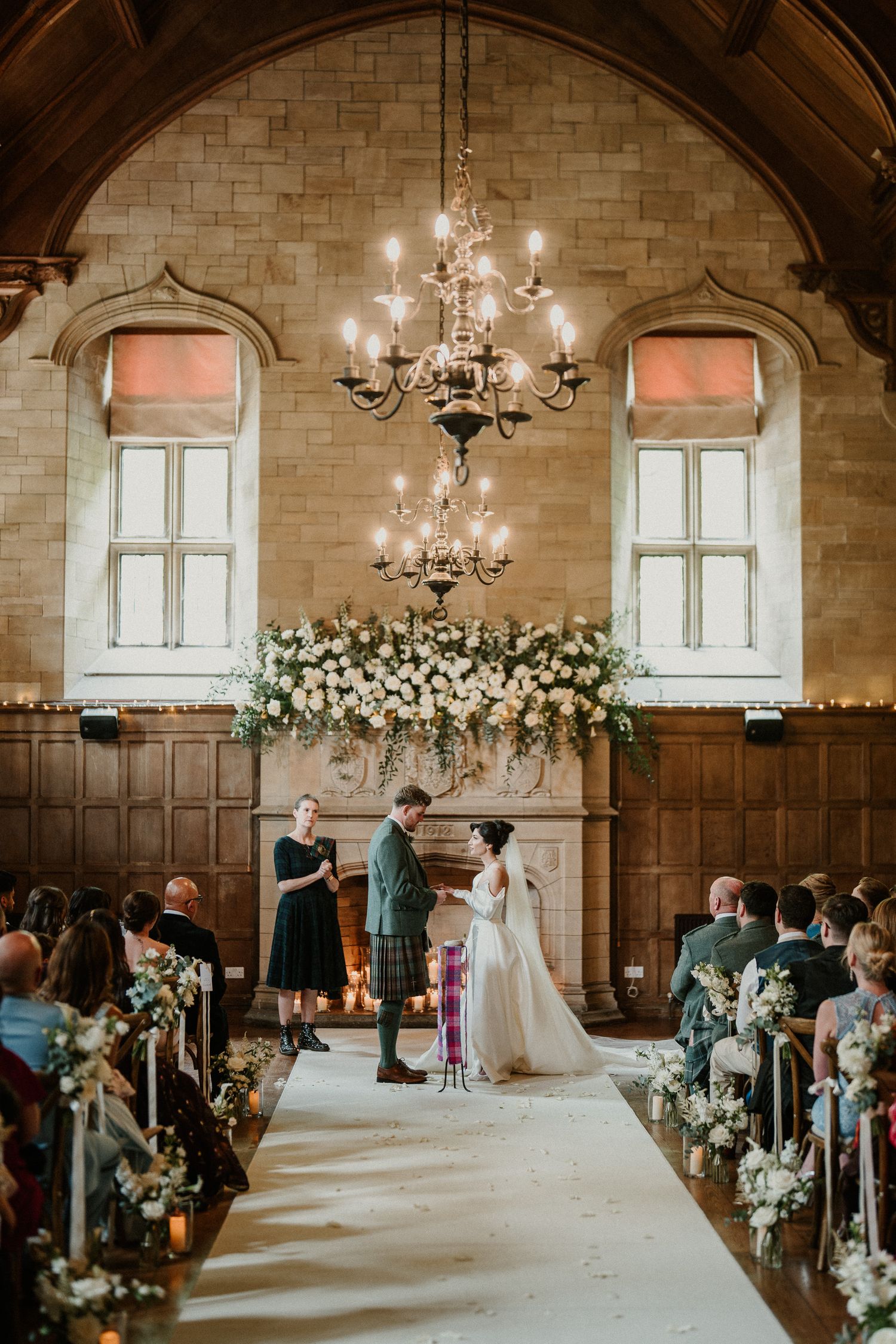 Church wedding ceremony with floral arch and chandeliers in historic stone interior.