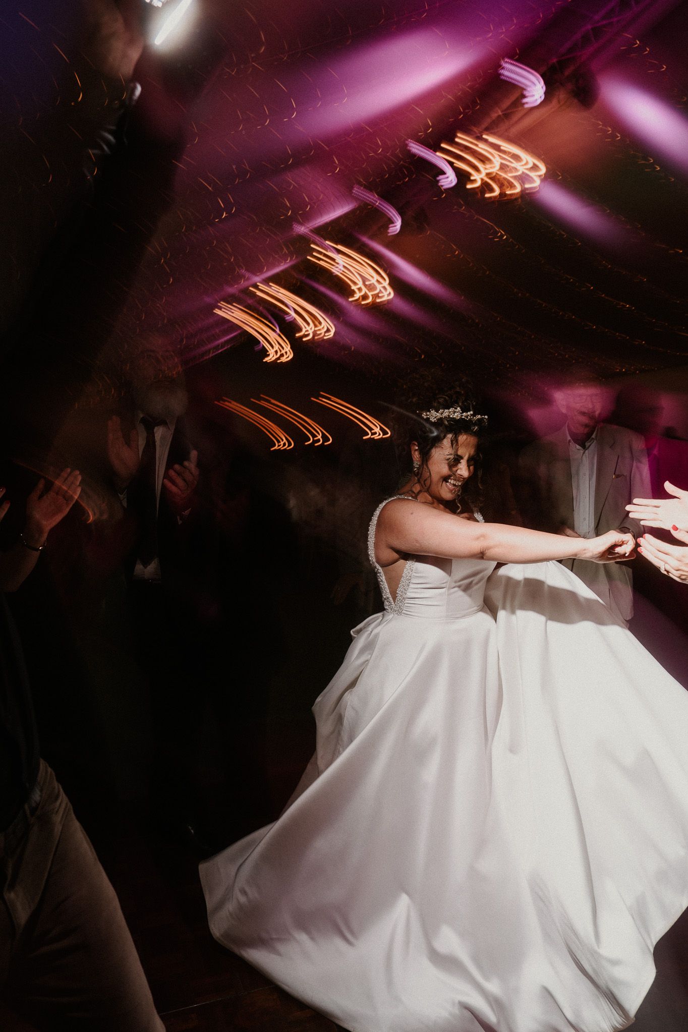 A bride in a flowing white dress twirling on the dance floor under dramatic purple lighting.