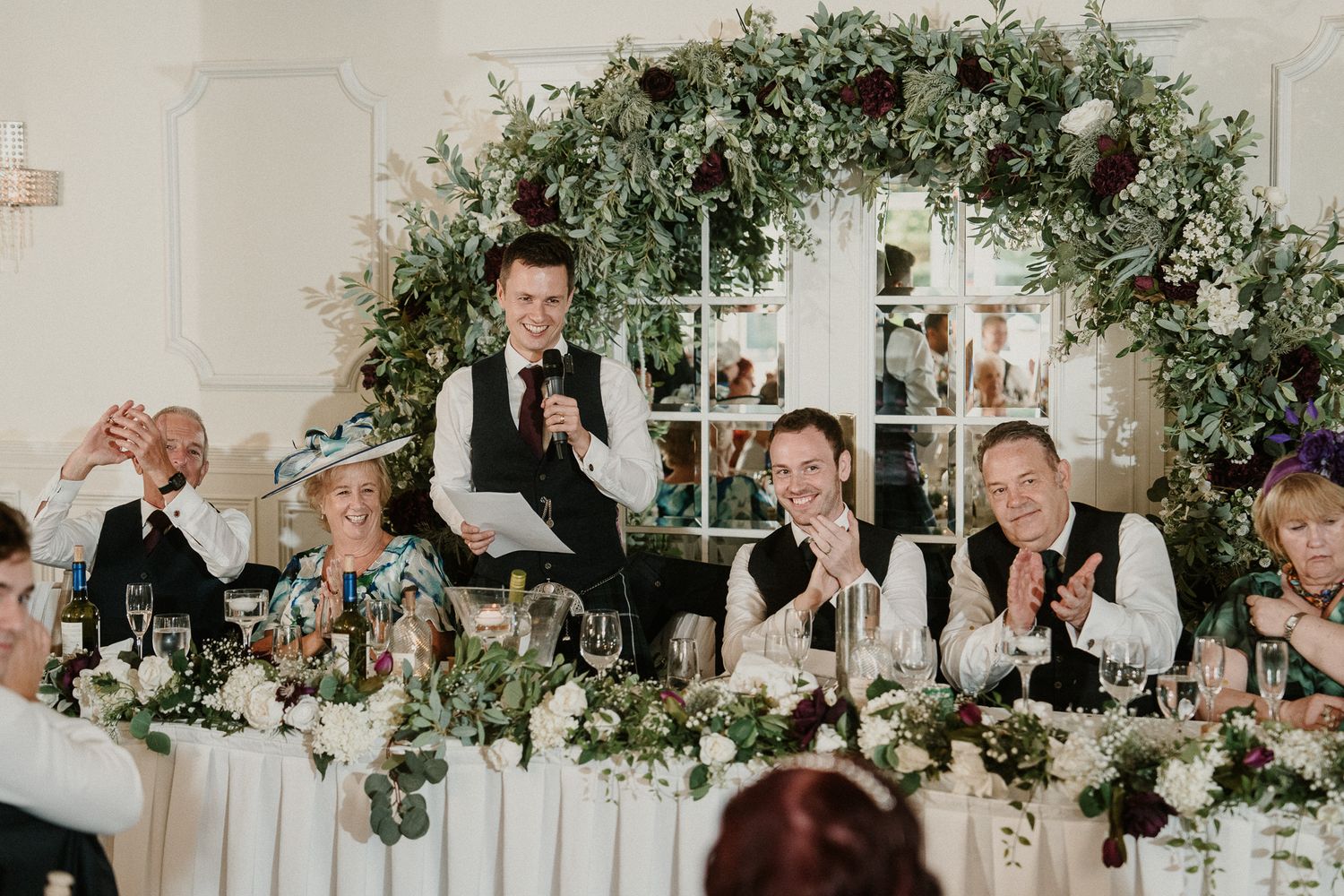 Wedding reception table decorated with greenery garlands and formal place settings.