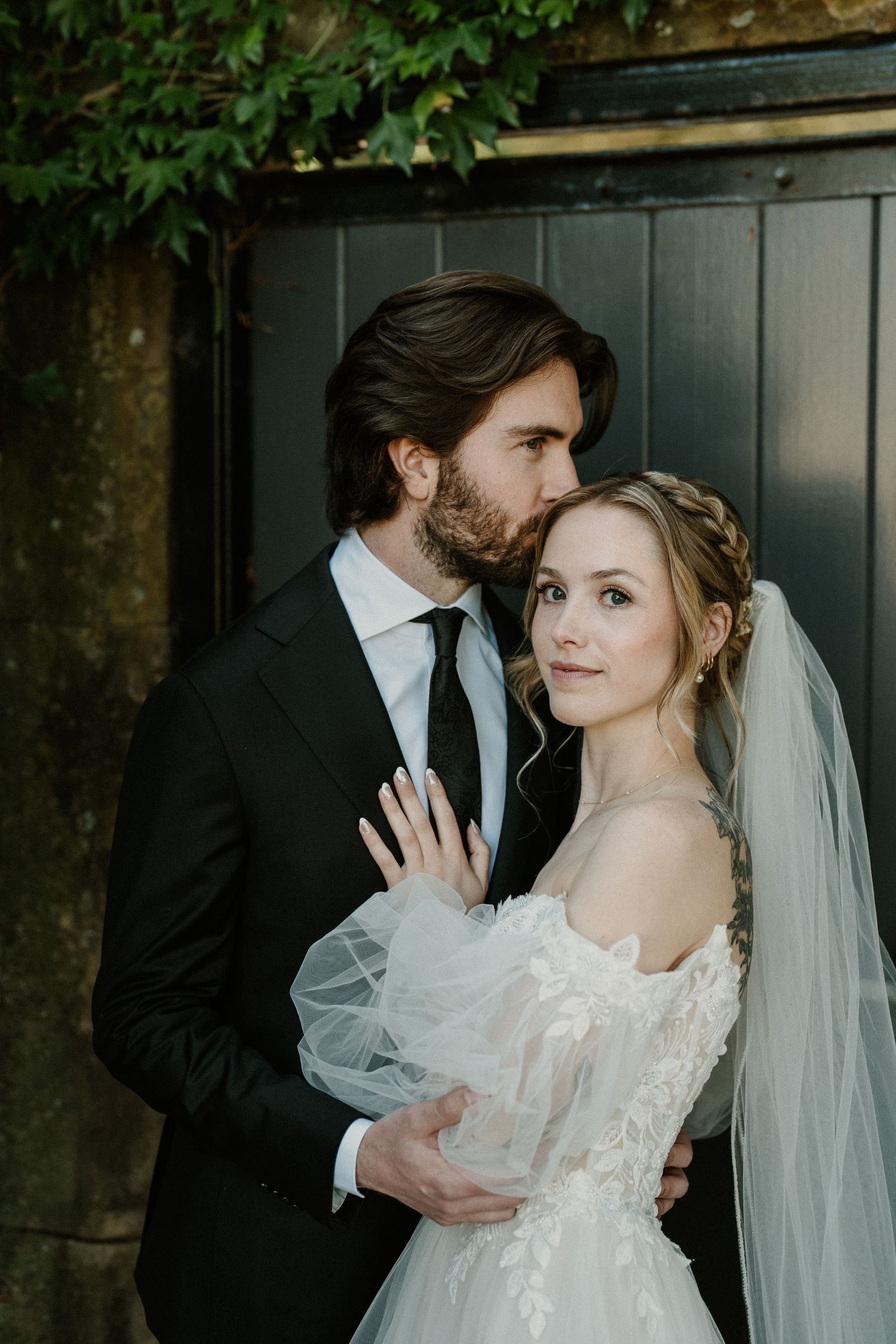 Artistic wedding portrait against dark wooden gate with natural greenery.