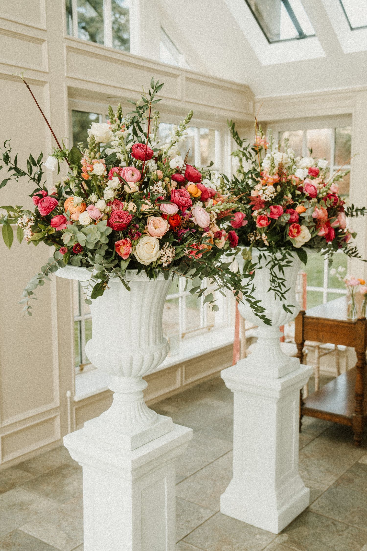 Elegant floral arrangements in white urns featuring pink and coral roses with greenery.
