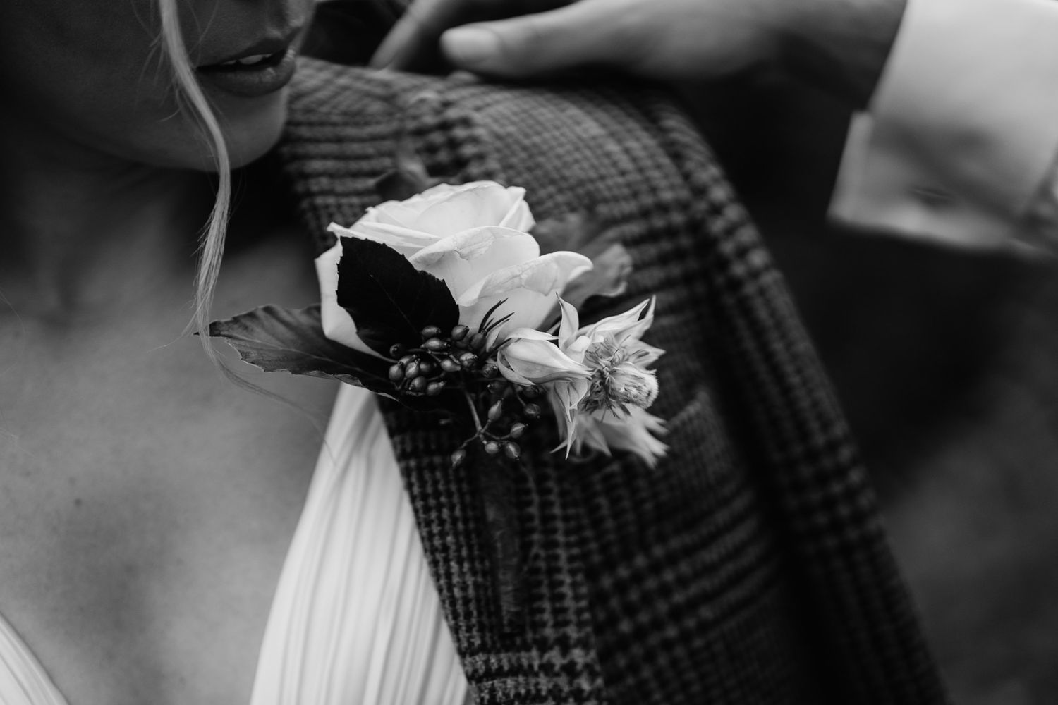 Close-up of delicate white floral boutonniere against tweed fabric.