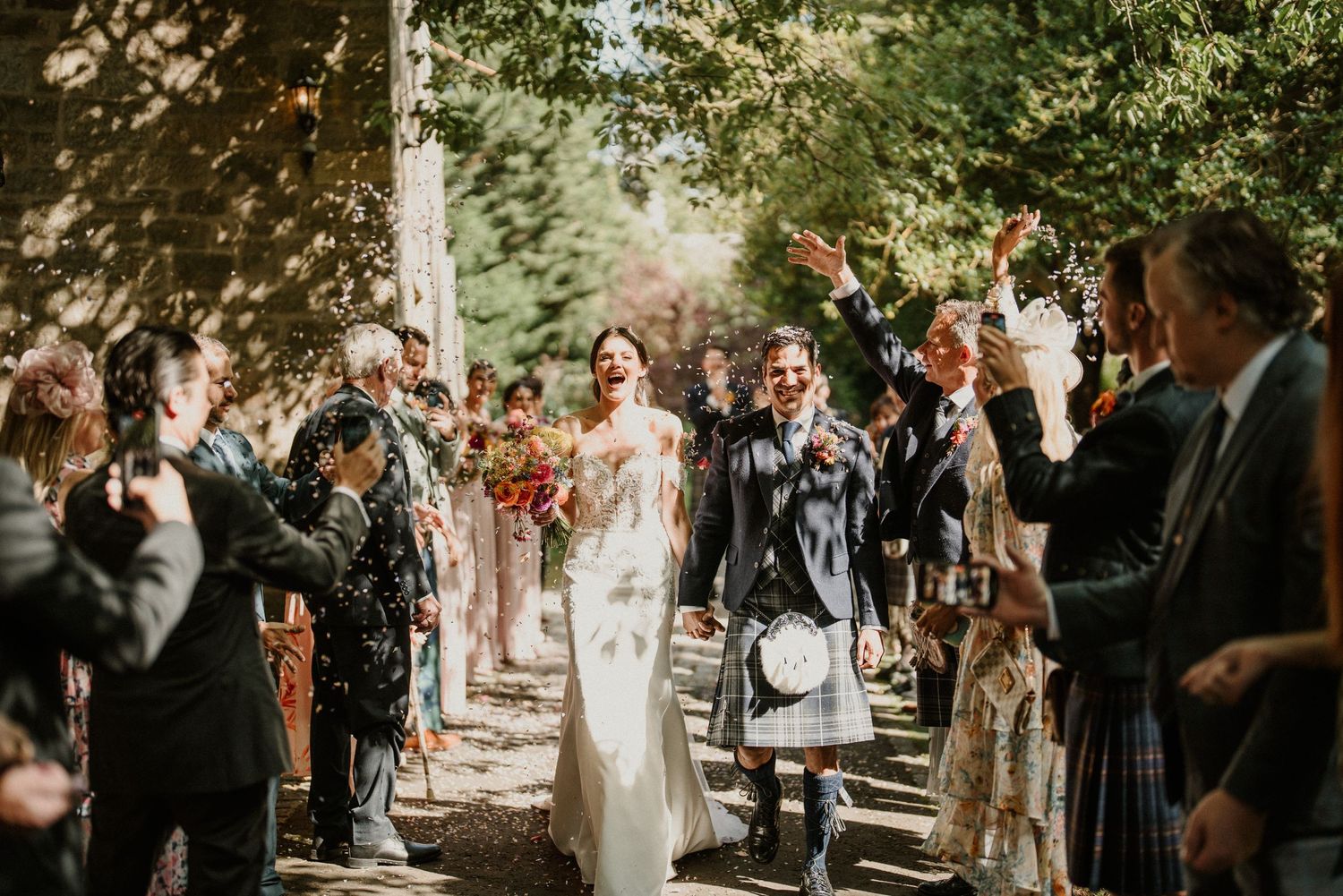 Wedding ceremony procession taking place on a sunlit outdoor path with guests watching.