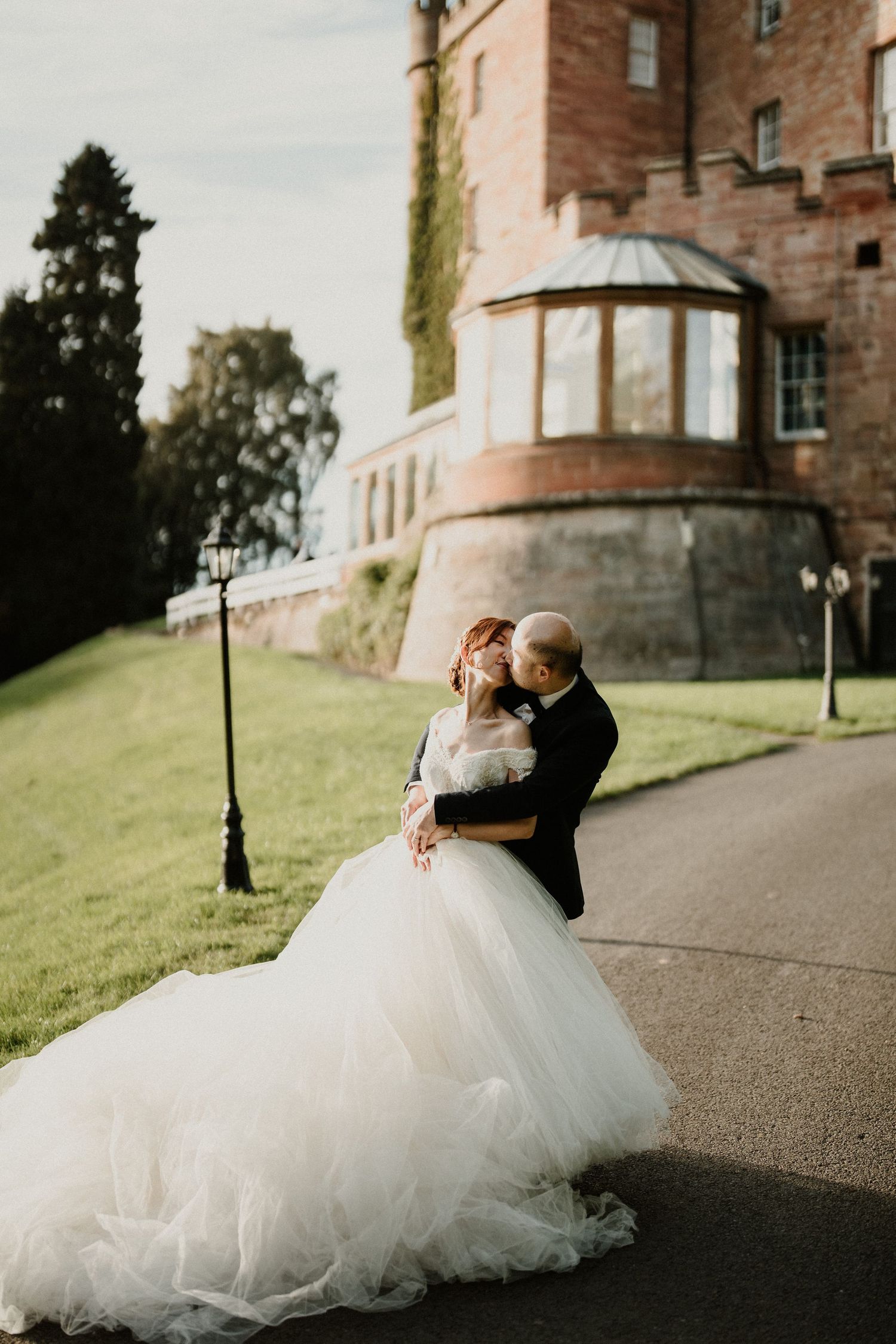 A couple shares an intimate dance moment on a path near a castle wall.