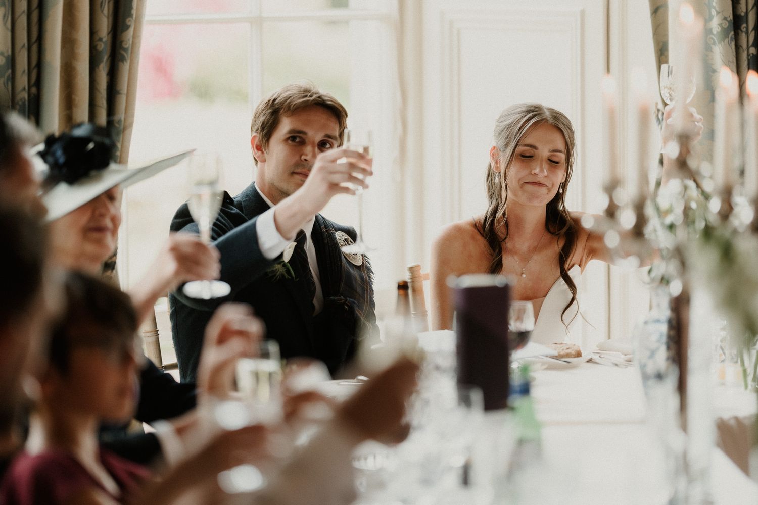 Bride and groom raising champagne glasses during wedding reception toast at elegant dining table.