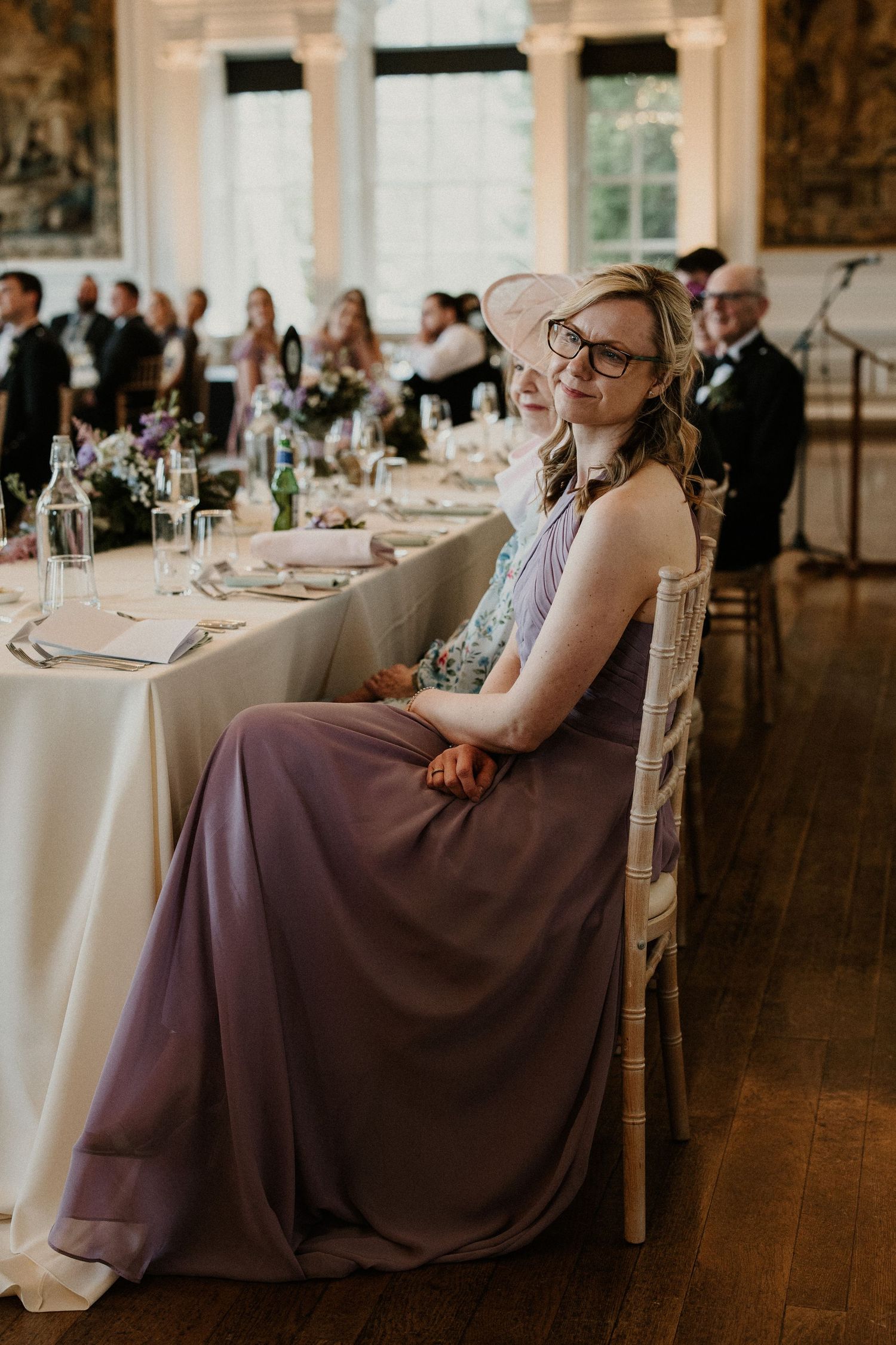 Wedding guest in purple dress seated at elegant reception table with formal place settings.