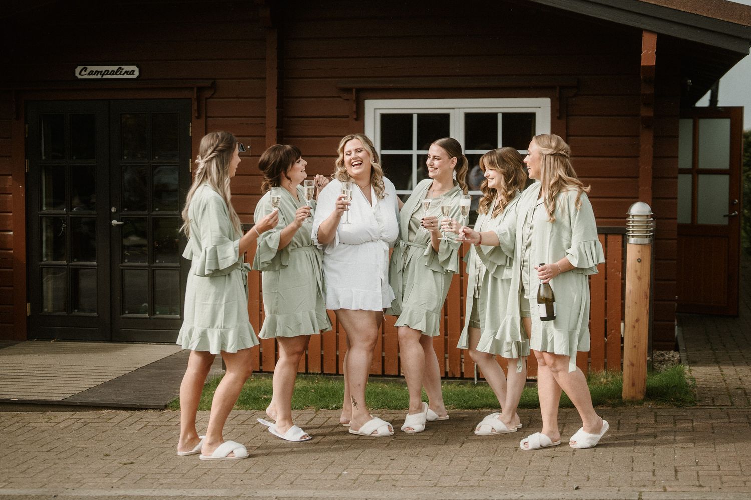 Group wearing coordinated white outfits stands outside brown wooden building.