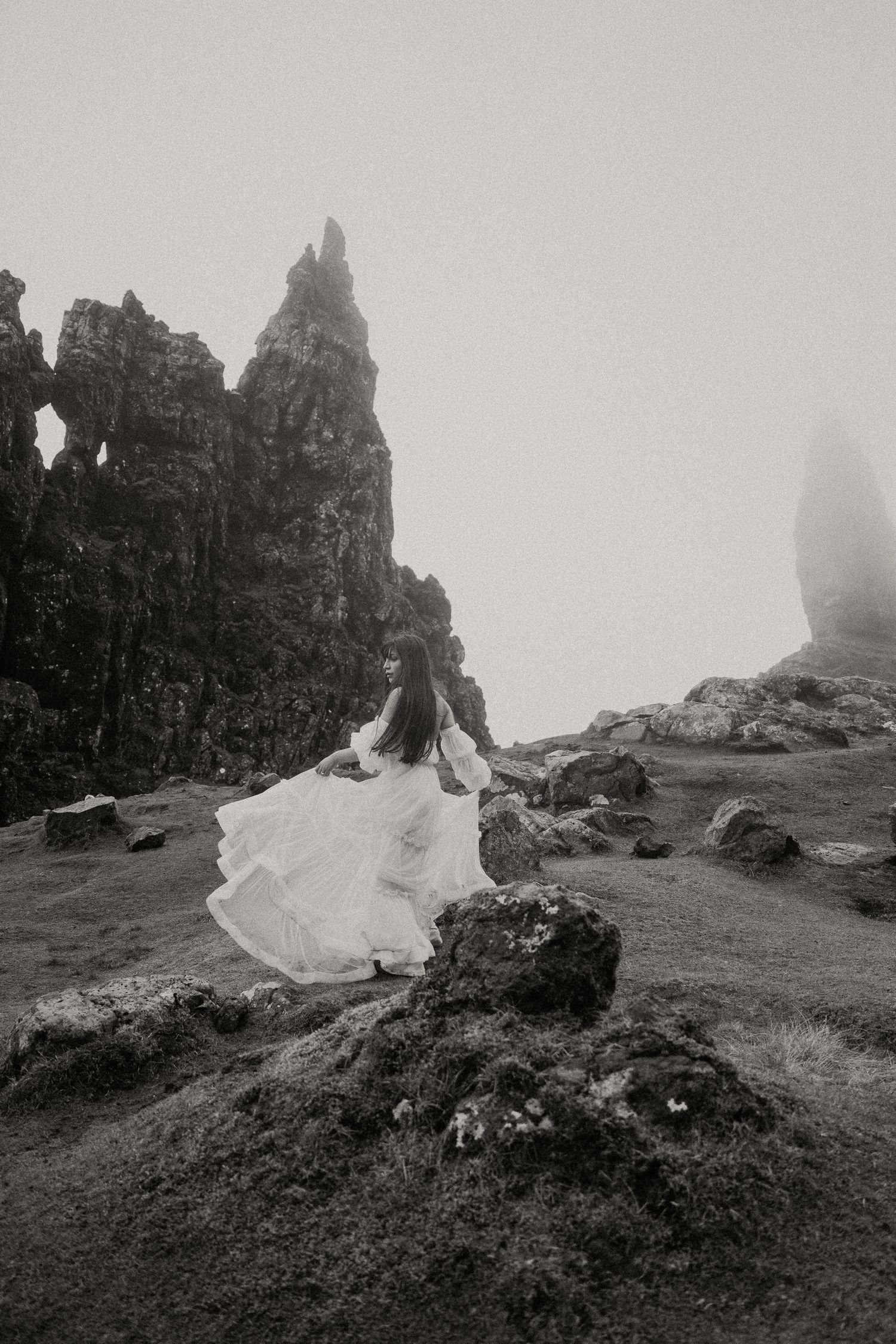Ethereal black and white photo of a flowing white dress billowing against rocky mountain spires.