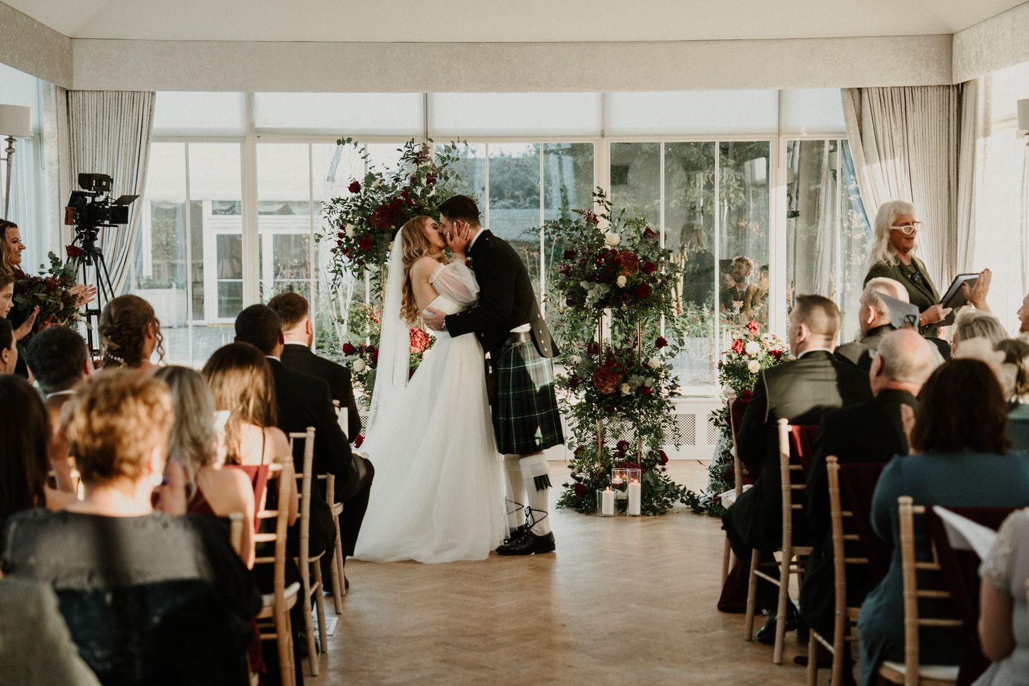 A wedding couple shares their first kiss during the ceremony as guests look on.