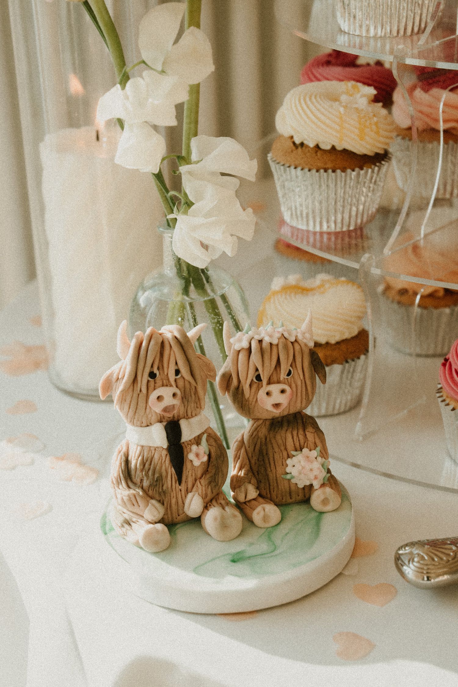 Cute decorative teddy bear cake toppers and cupcakes displayed on white pedestals at a wedding reception.