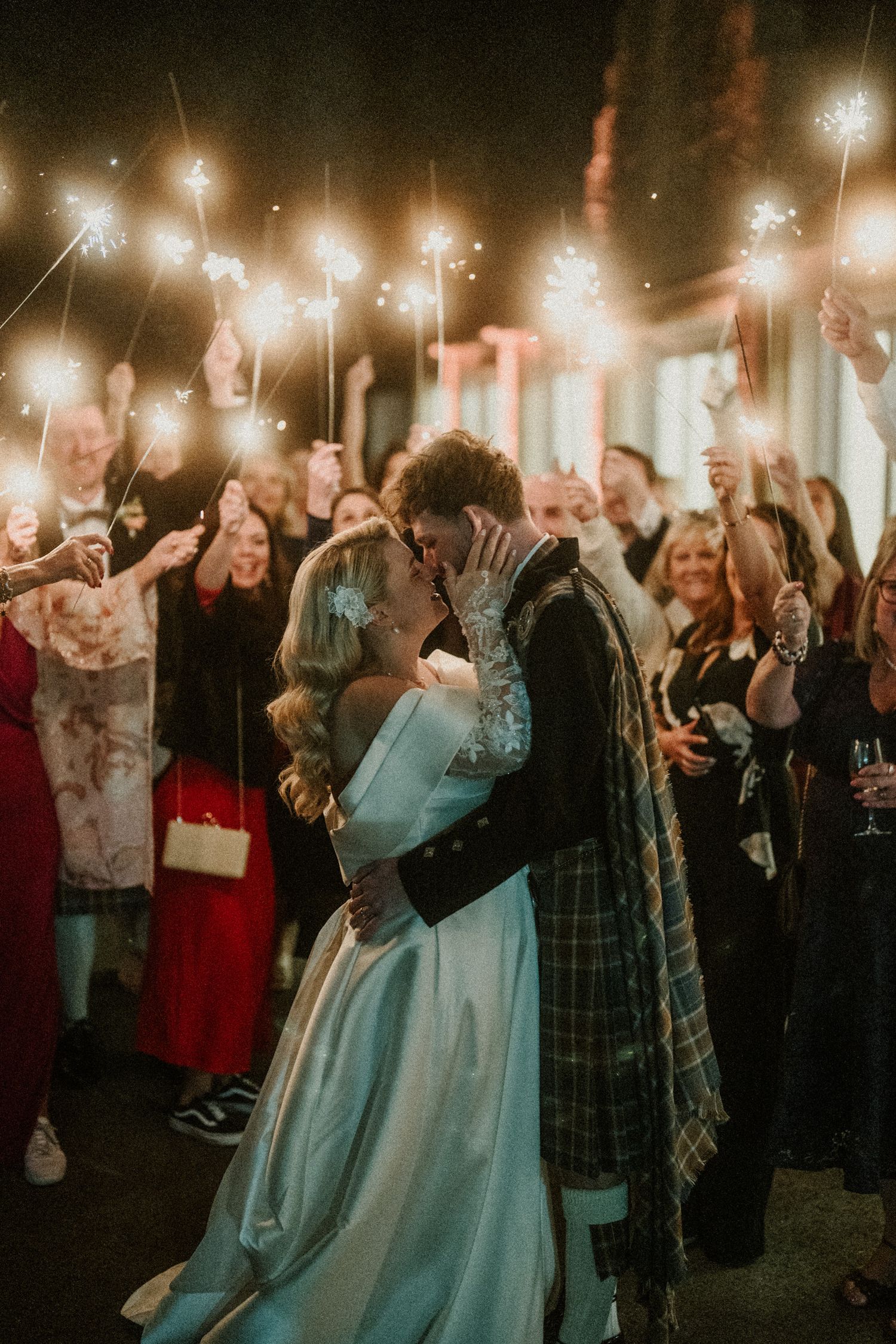 Romantic sparkler moment during evening wedding reception with guests celebrating.
