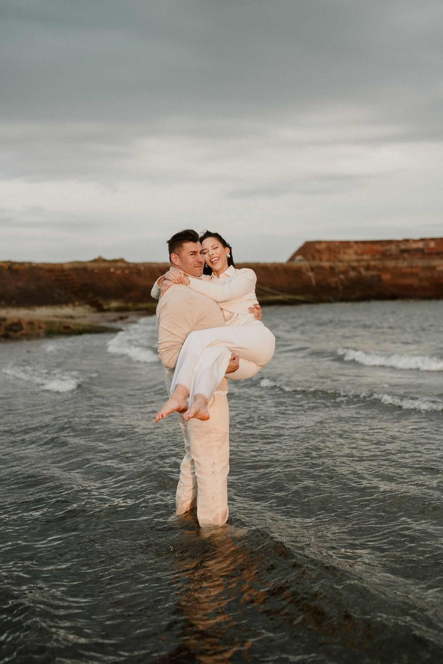 Couple in light colored clothing sharing an intimate moment while standing in shallow ocean water.