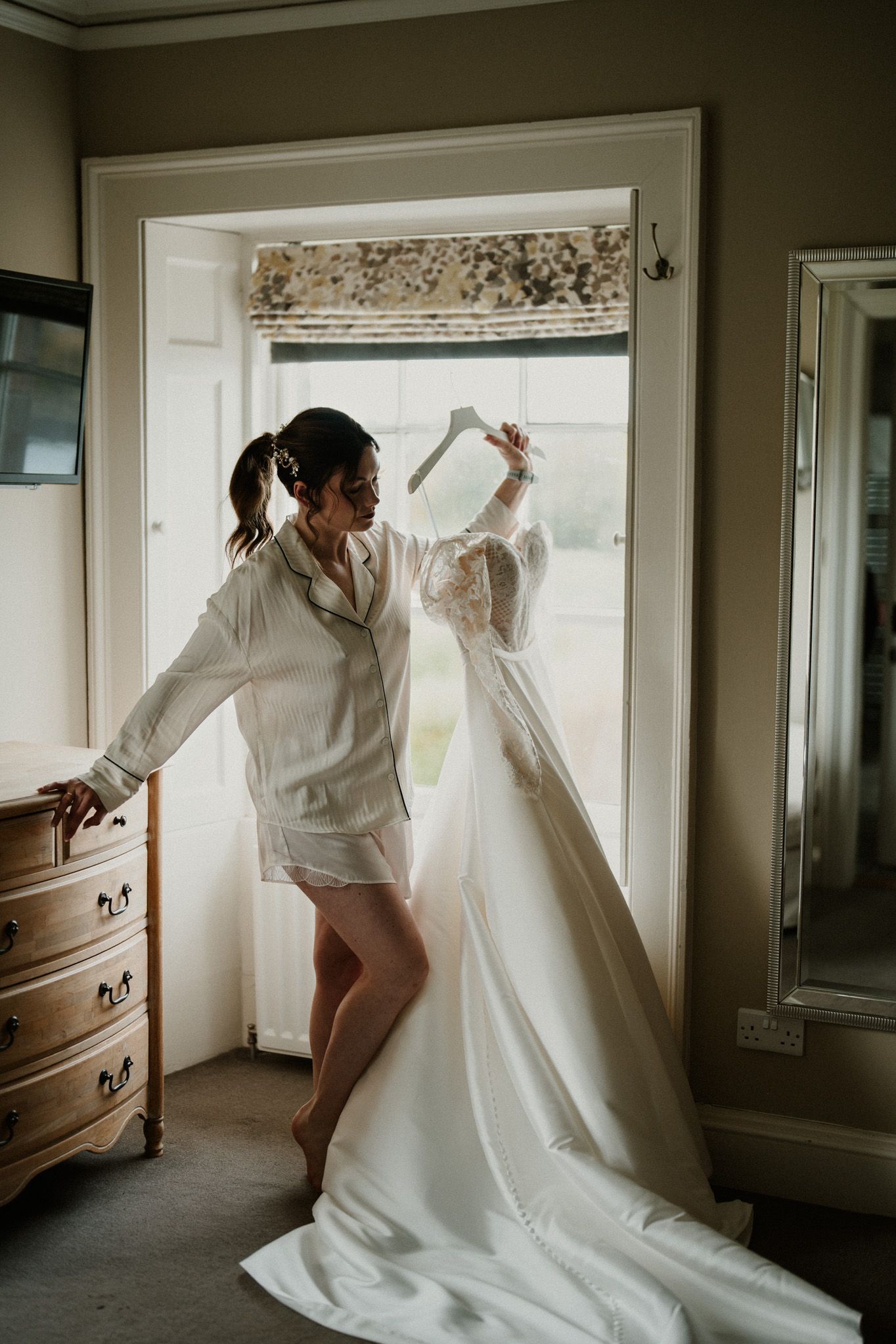 Artistic series of someone playfully interacting with a hanging wedding gown near a window.