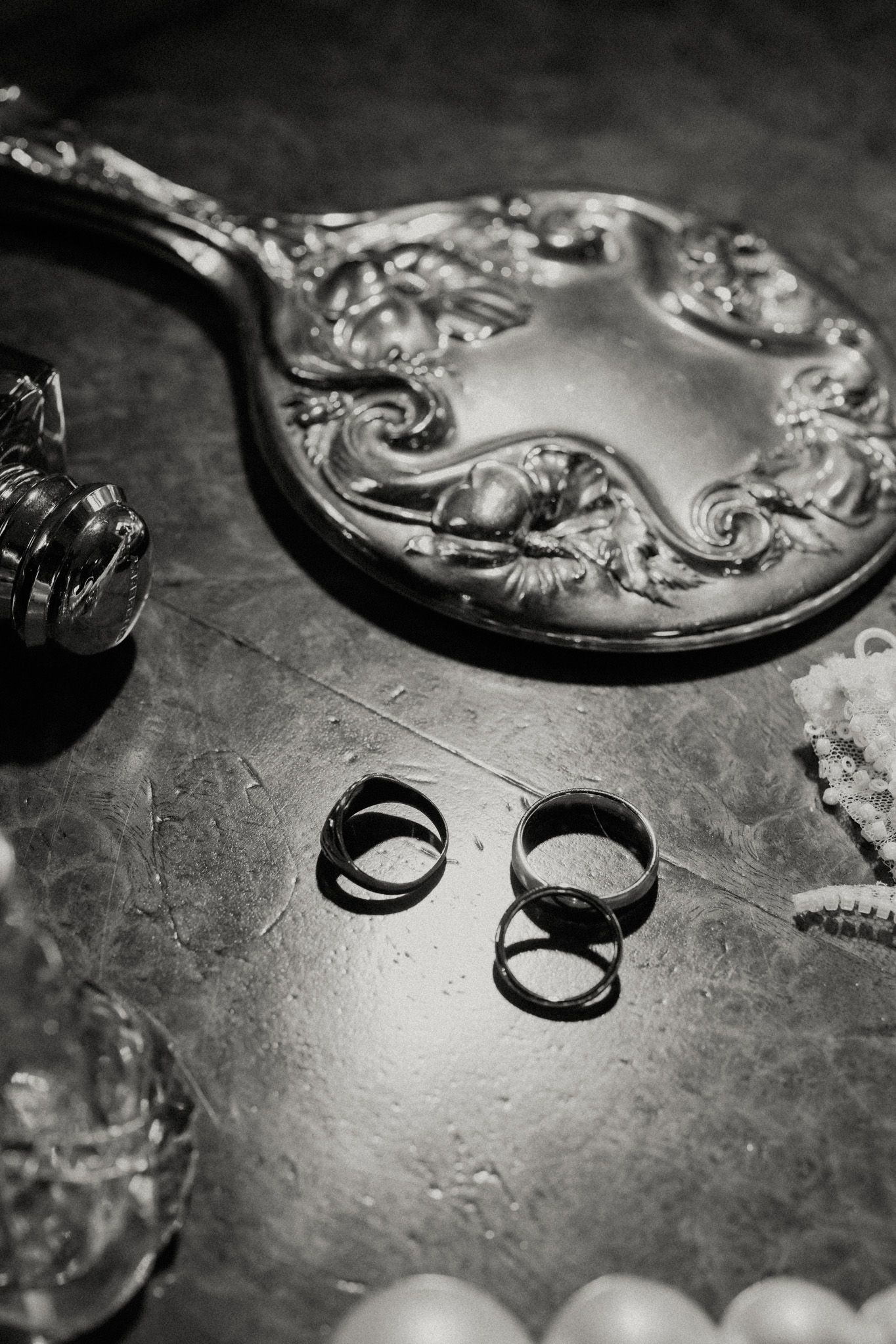 Black and white close-up of wedding rings beside decorative silver mirrors.