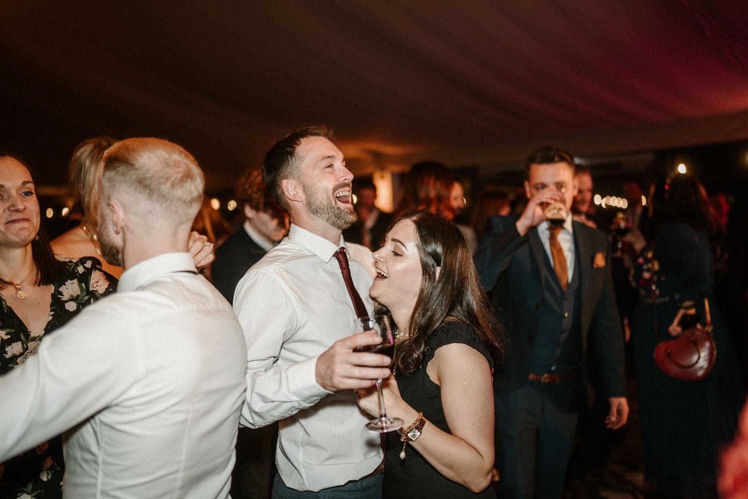 Wedding guests laughing and dancing together during a lively reception celebration.