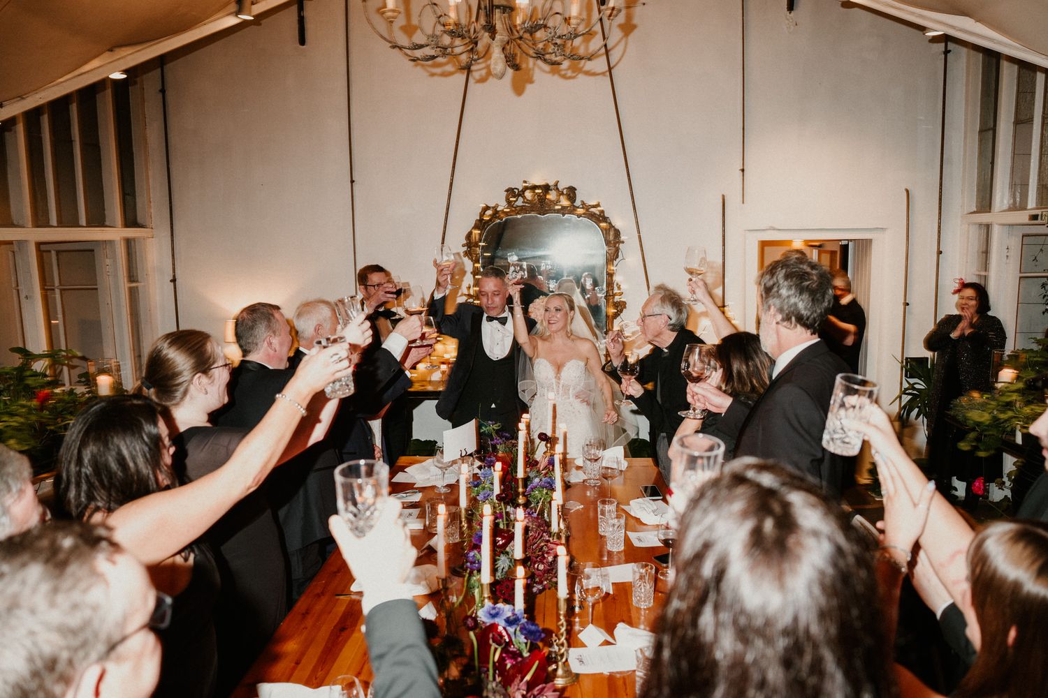 Celebratory toast moment at an elegant indoor wedding reception with chandelier lighting.