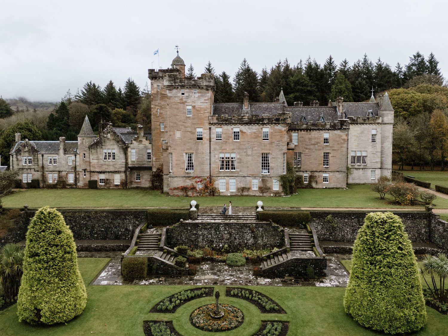 Historic stone castle estate with manicured gardens, topiary bushes, and decorative stone bridges in Scotland.