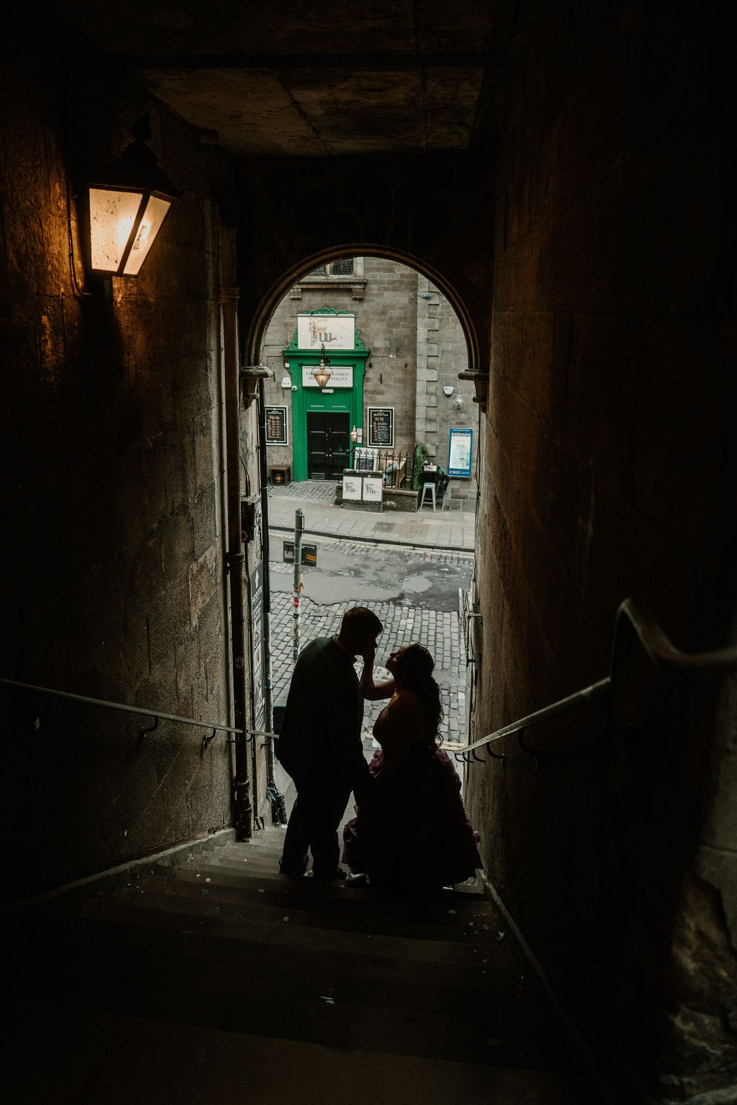 Silhouetted couple sharing a romantic moment in a dark stone archway passage in Edinburgh's Old Town.
