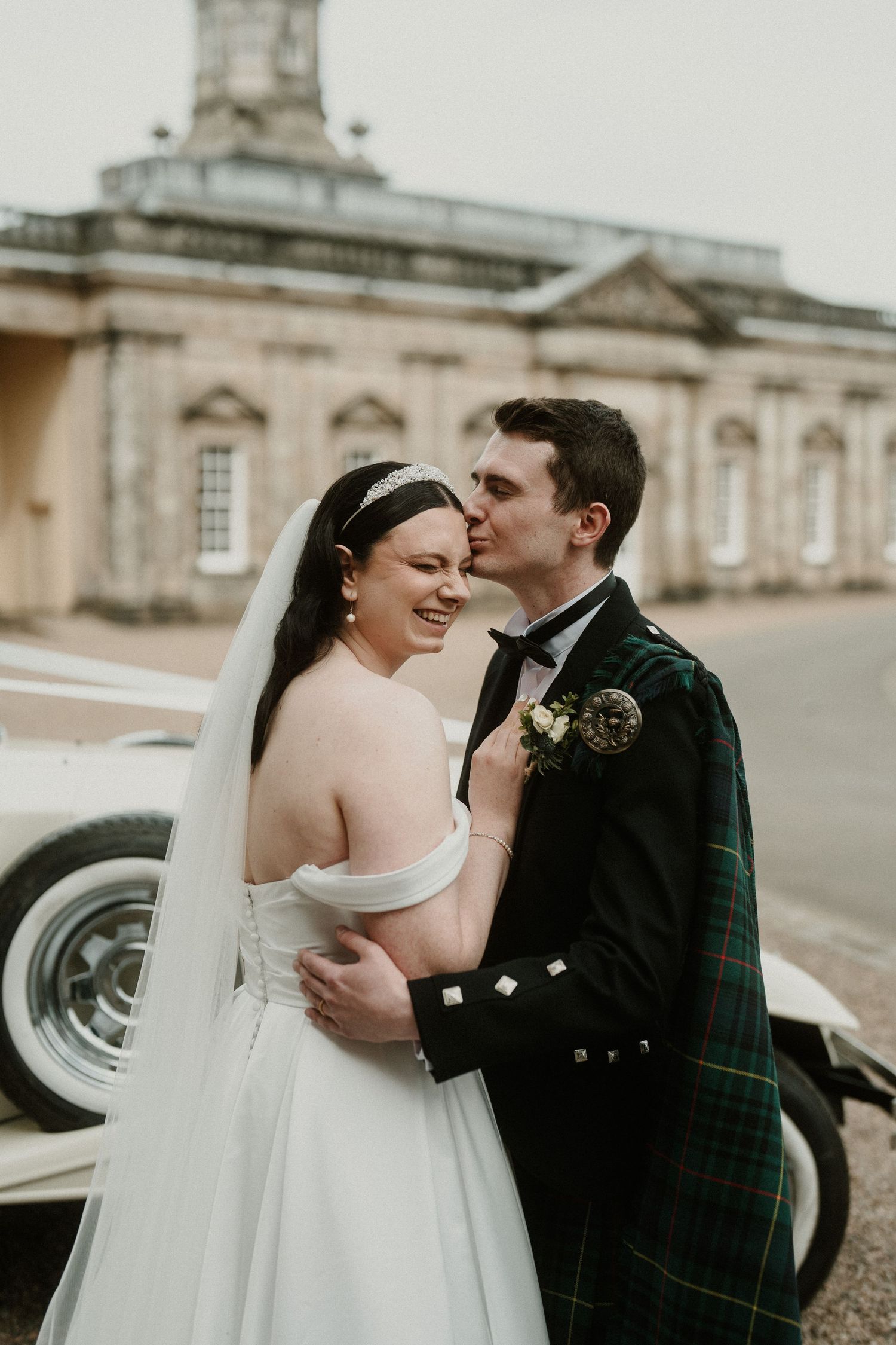 Romantic wedding portraits with couple in traditional Scottish attire by vintage car.