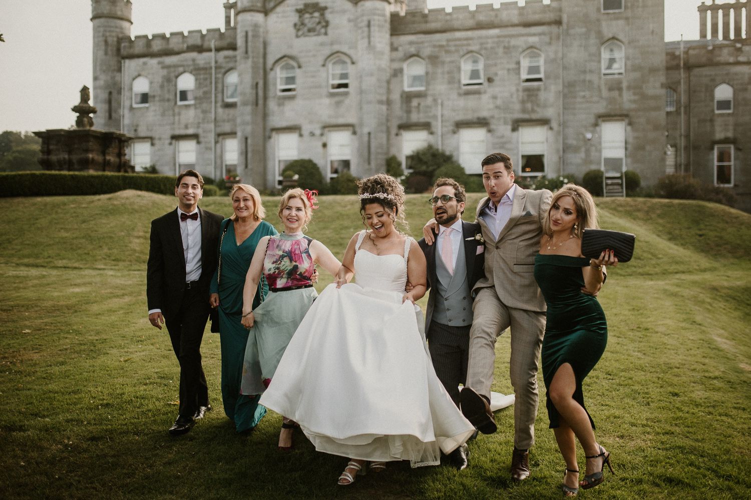 Wedding party celebrates on castle grounds with historic architecture in background.