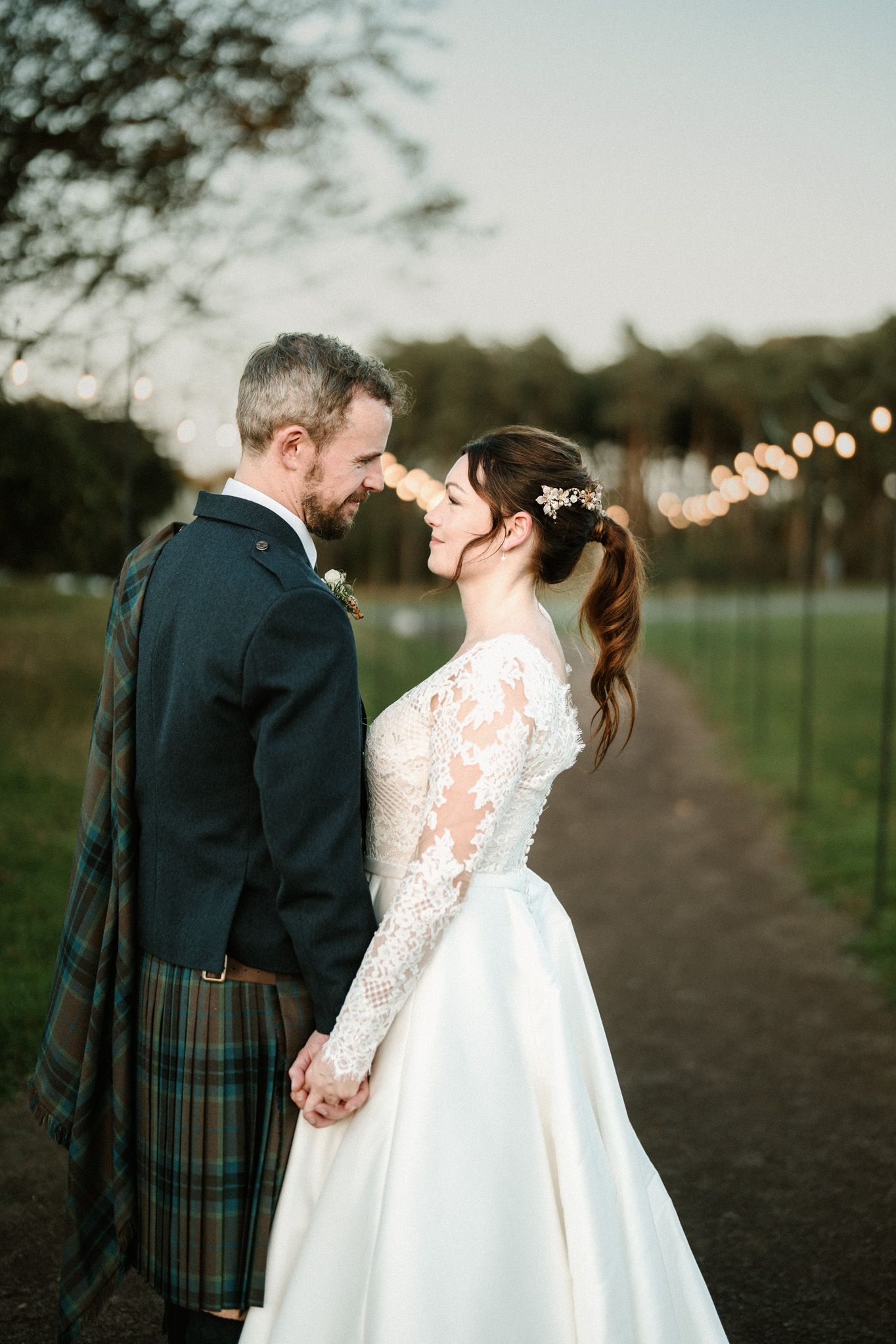 Couple in traditional Scottish wedding attire sharing intimate moments on a countryside path.
