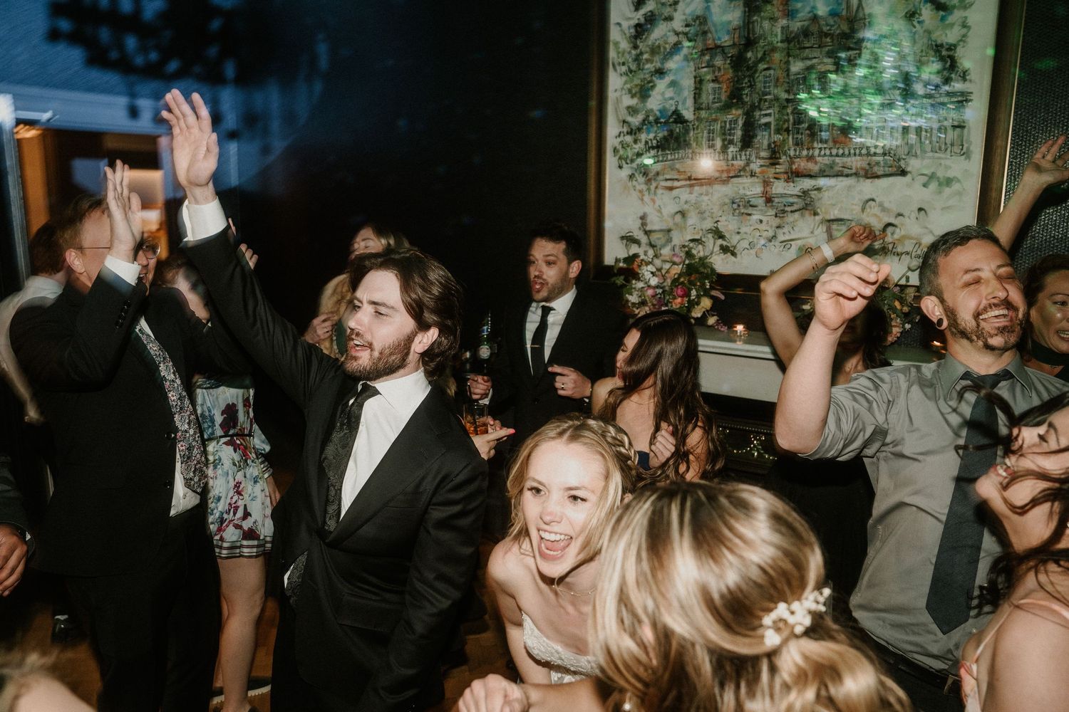 Wedding reception guests dancing and celebrating on a dark dance floor with atmospheric lighting.
