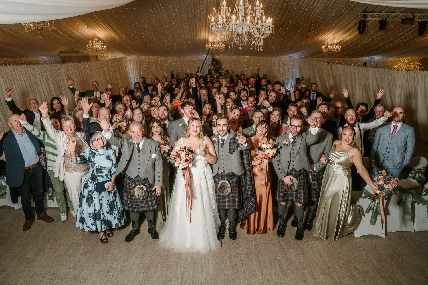 Wide shot of wedding reception hall filled with guests and elegant decor.