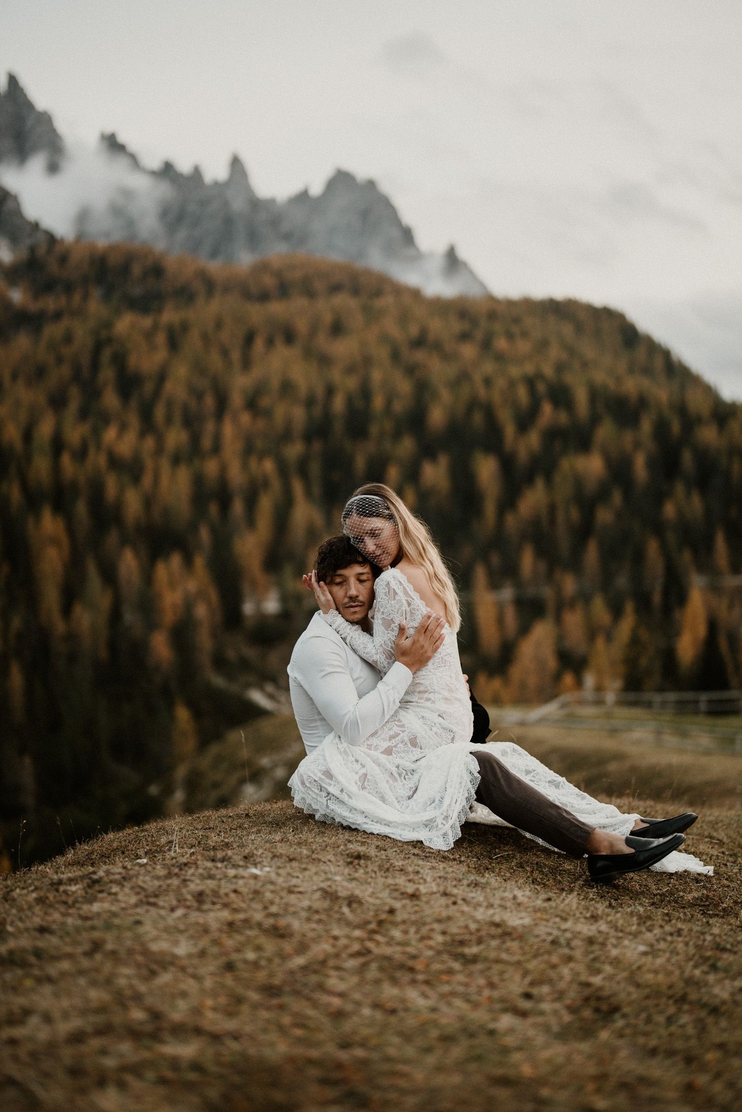 A romantic couple in white outfits share an intimate moment against a backdrop of autumn mountains and forests.