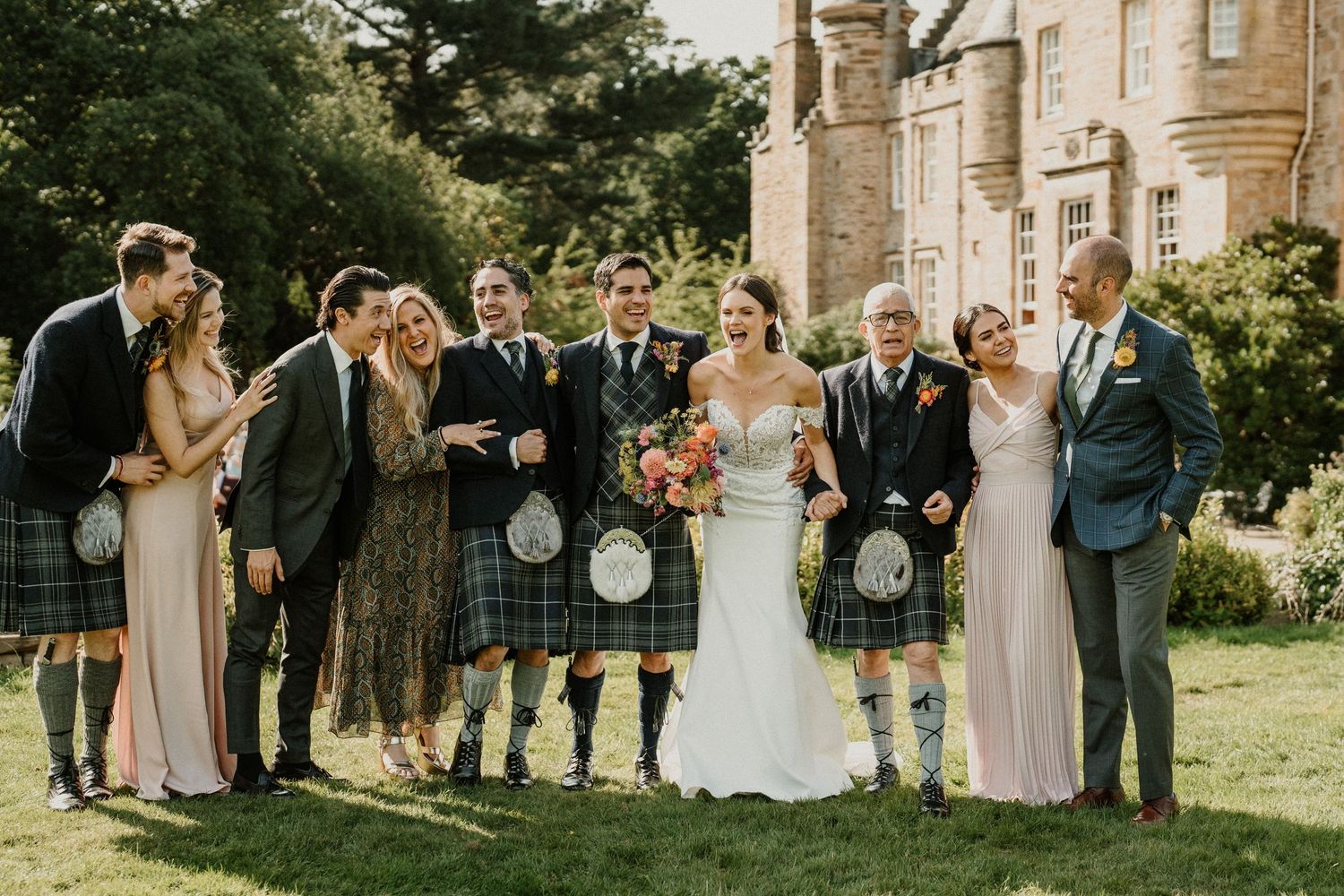 Wedding group photo session outside majestic Scottish castle on sunny day.