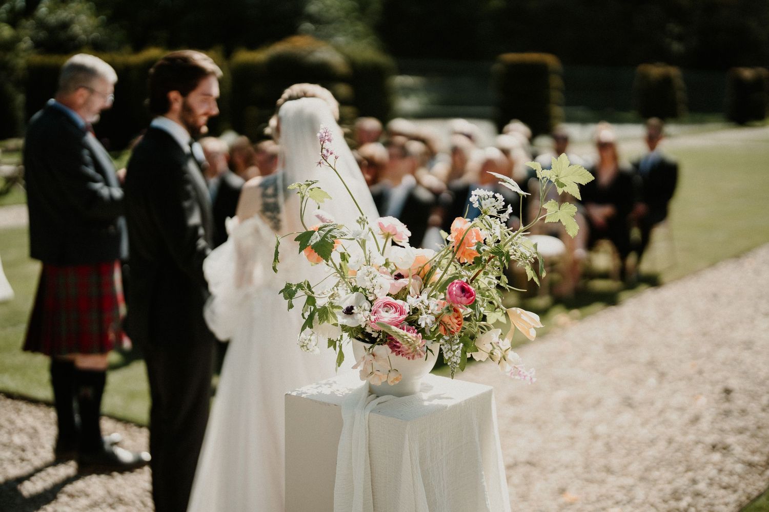 Outdoor wedding ceremony setup with white pedestals and pink floral arrangements.