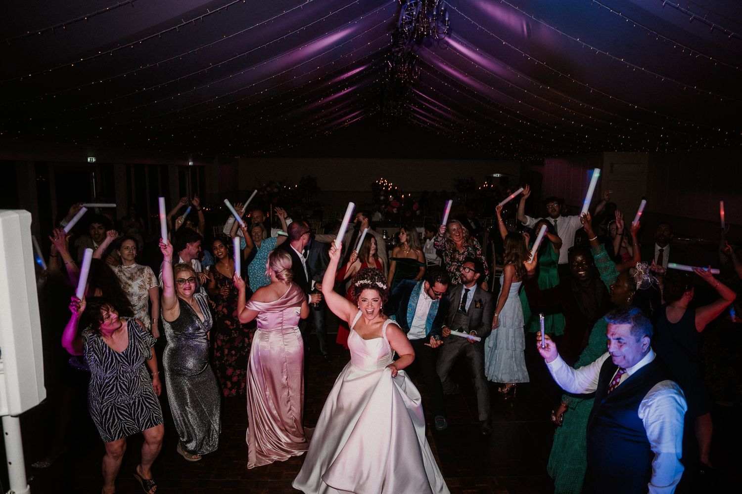 Wedding celebration with guests dancing under dramatic purple mood lighting.