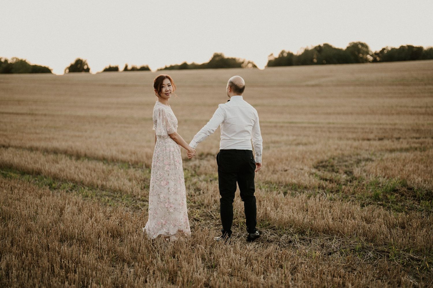A romantic couple poses in a golden wheat field during sunset.