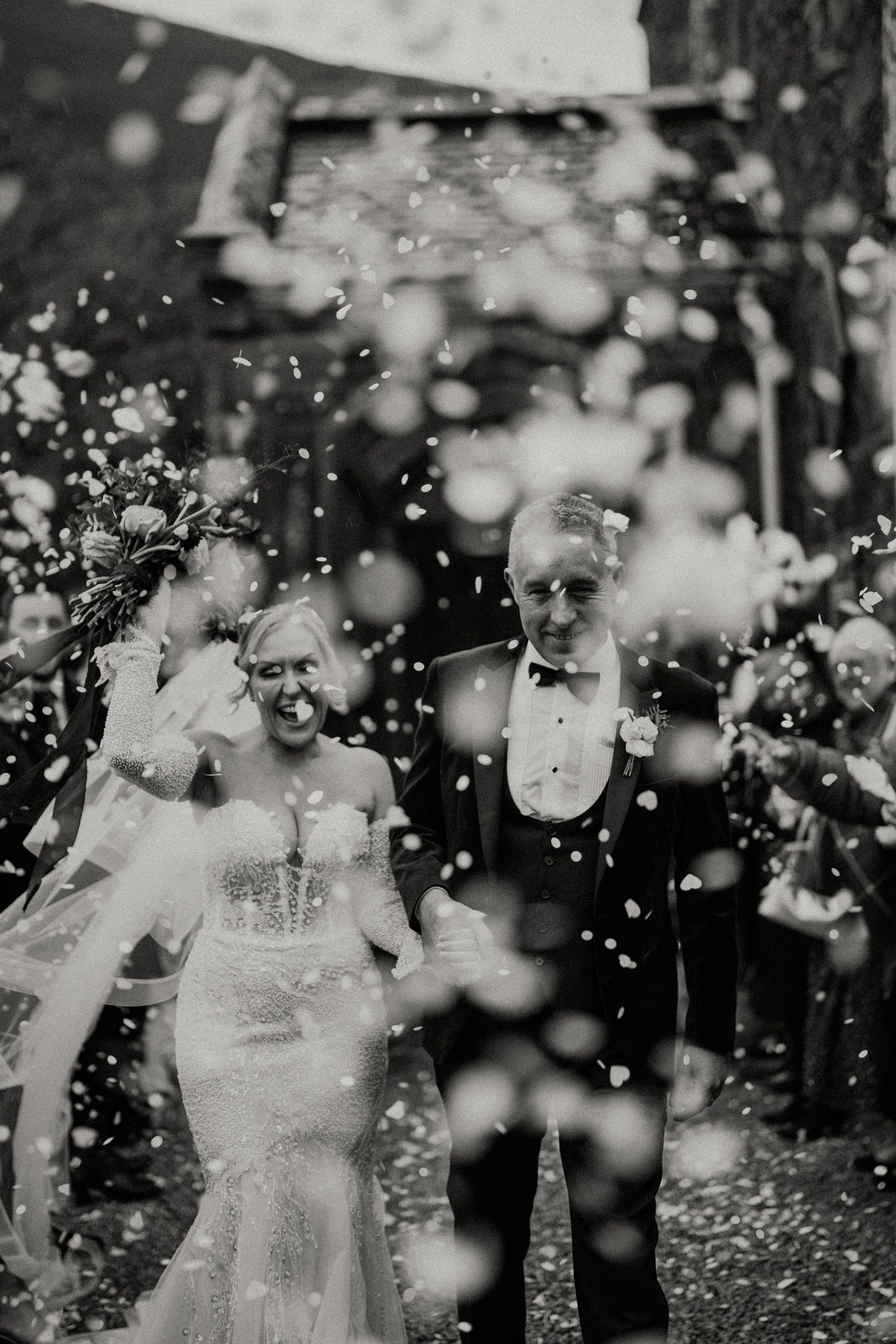Black and white photo of newlyweds walking through confetti after their wedding ceremony.