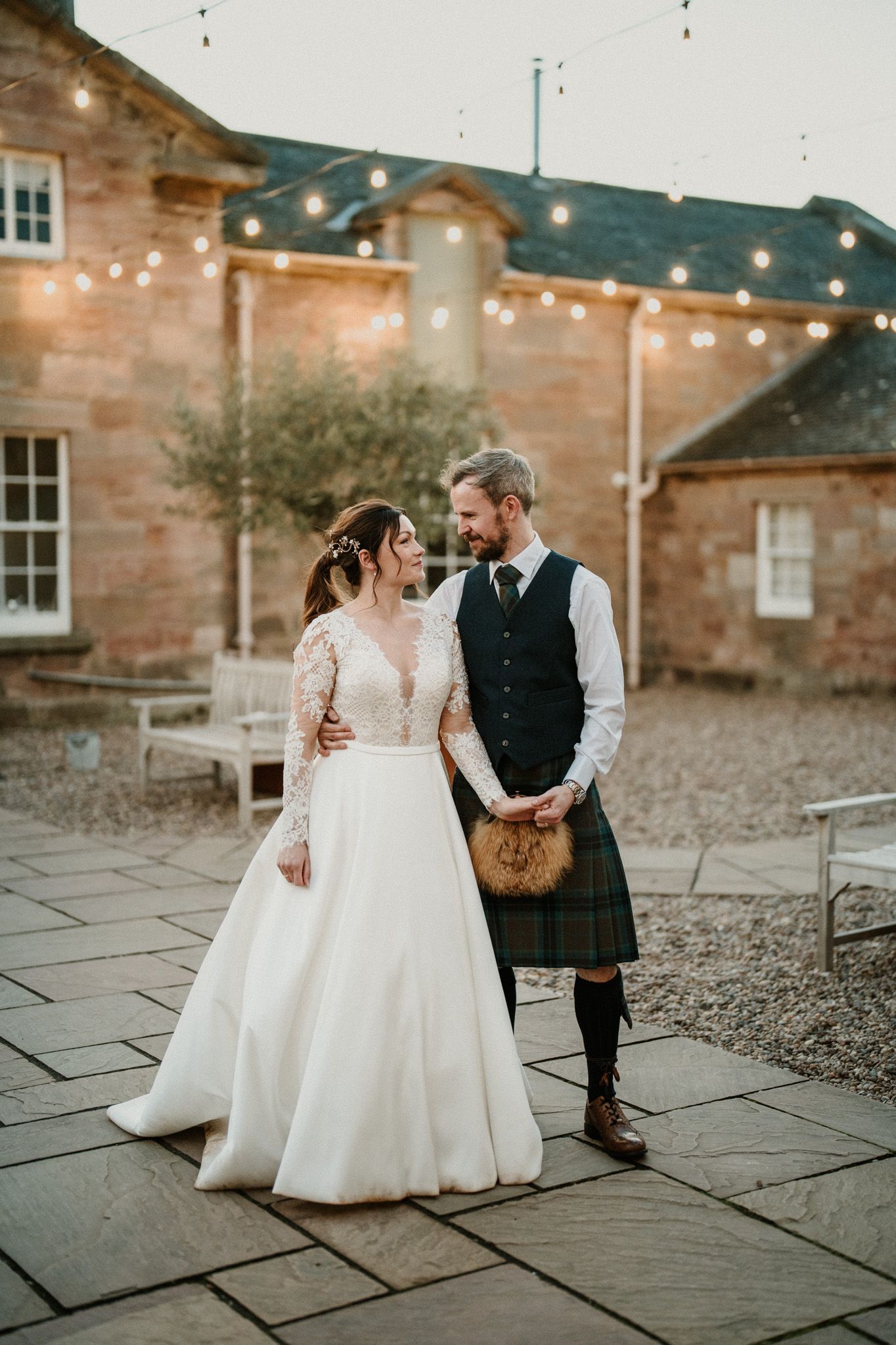 Couple dancing outside historic stone building with string lights overhead.