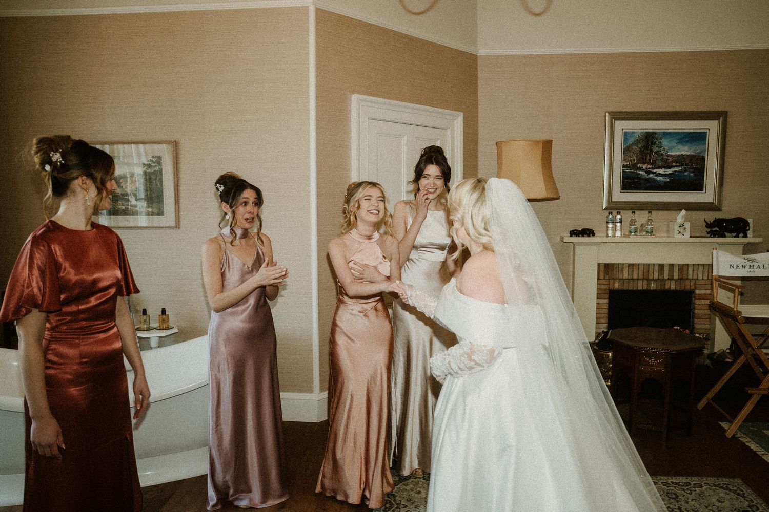 Wedding party members in burgundy and blush dresses help arrange the bride's gown.