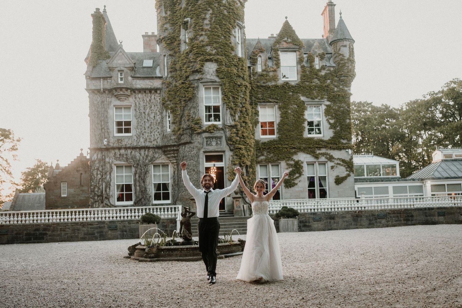 A couple walks along the grounds of a majestic stone castle estate.