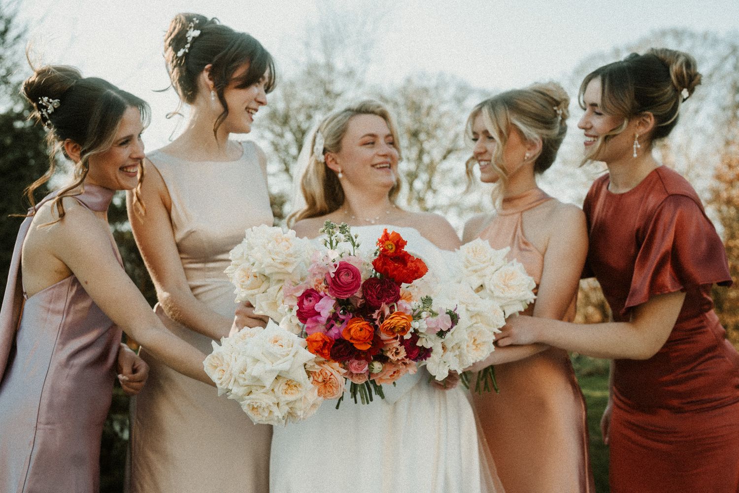 Joyful bridal party shares candid moment with bouquets in autumn wedding setting.