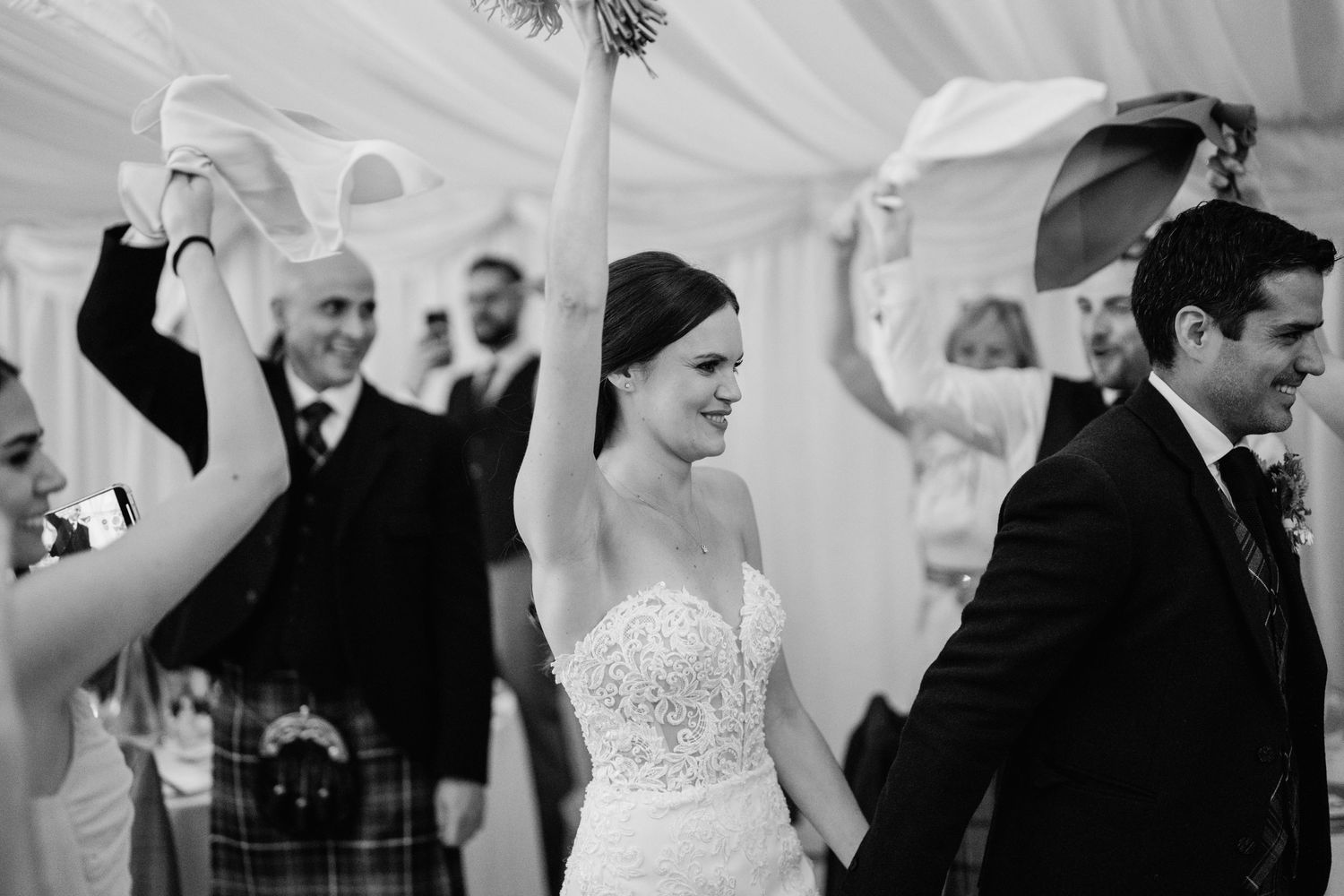 Joyful celebration under white tent during Scottish wedding reception.