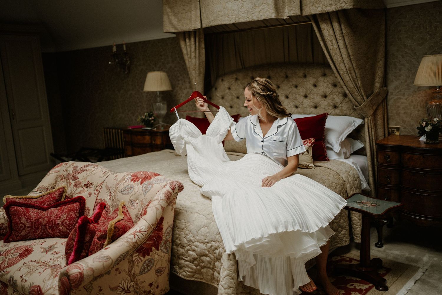 A wedding dress is displayed on a luxurious bed with vintage decor and warm lighting.