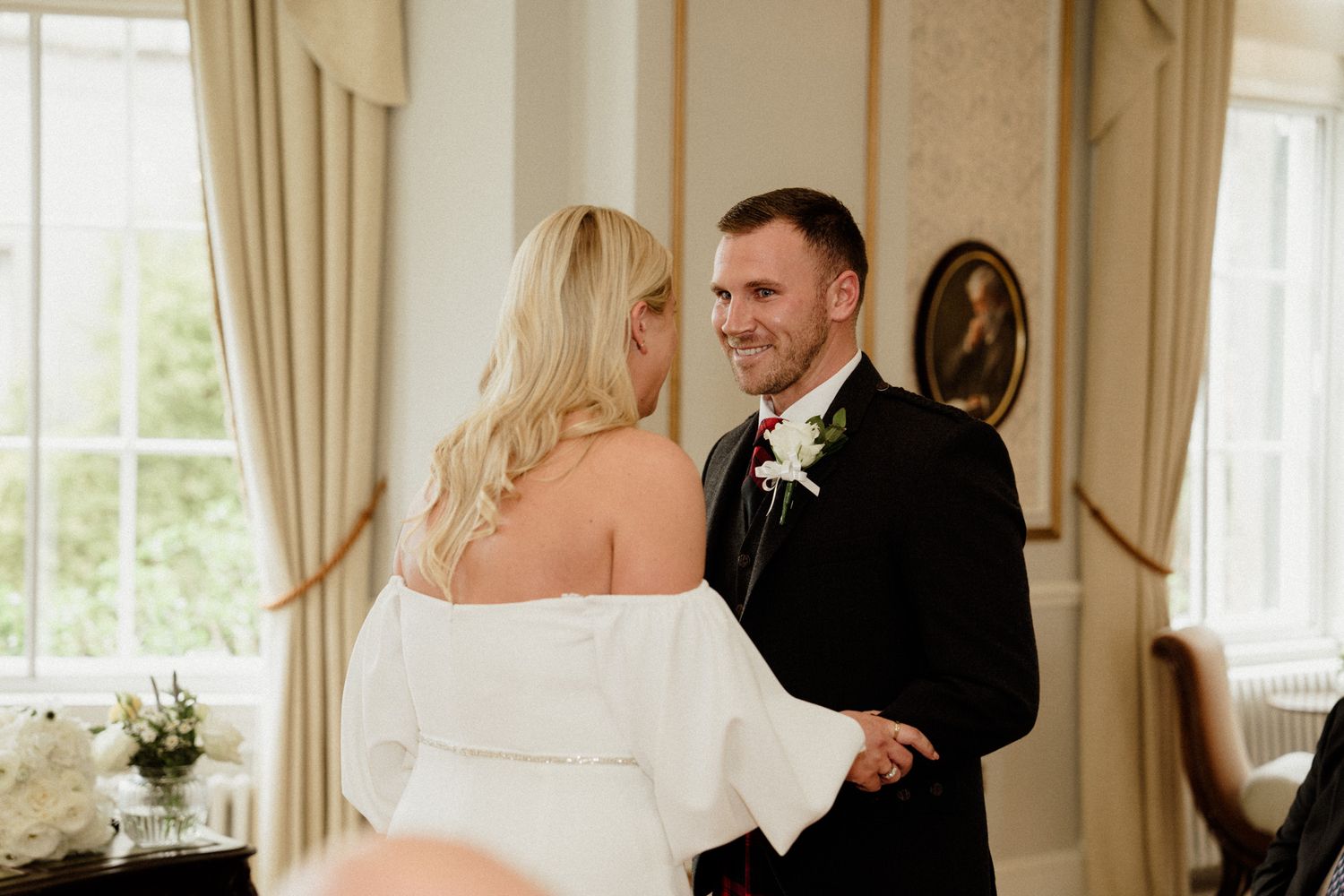 Elegant wedding couple shares intimate moments in a classically decorated room with large windows.