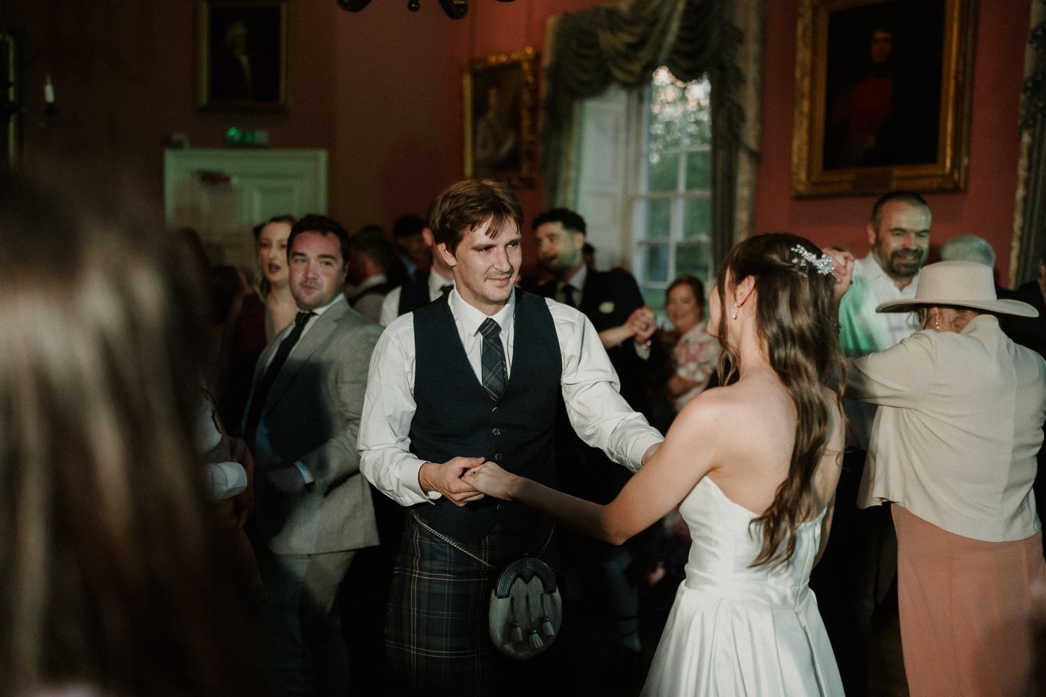 Bride and groom share a dance at elegant Scottish castle wedding reception, groom wearing traditional kilt.