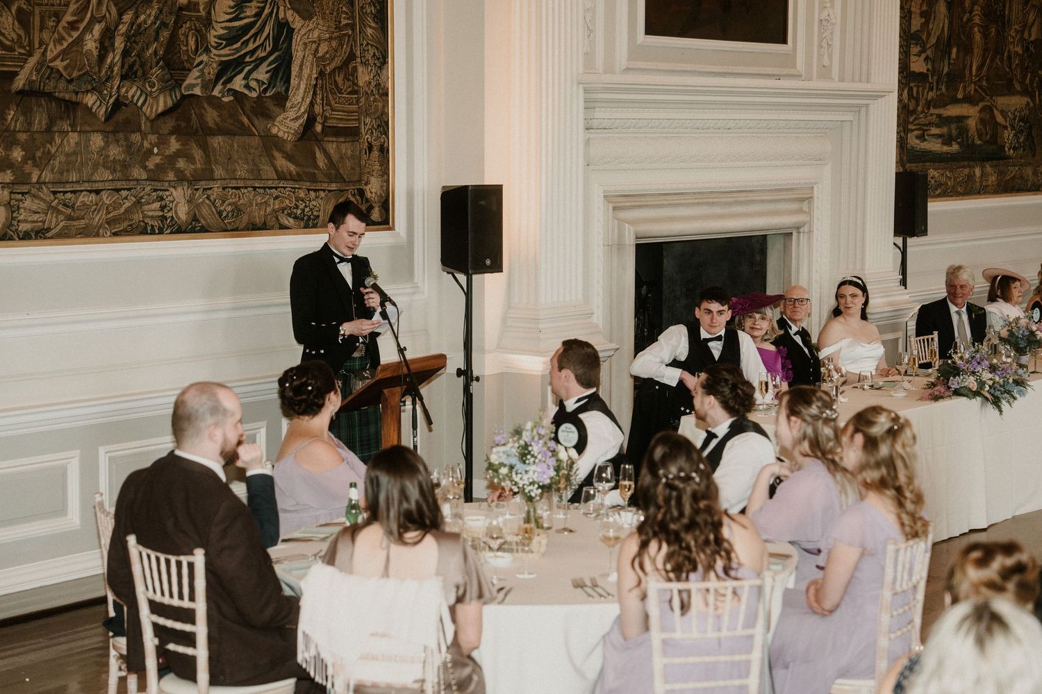Wedding reception speeches being given in an ornate room with tapestry-covered walls.