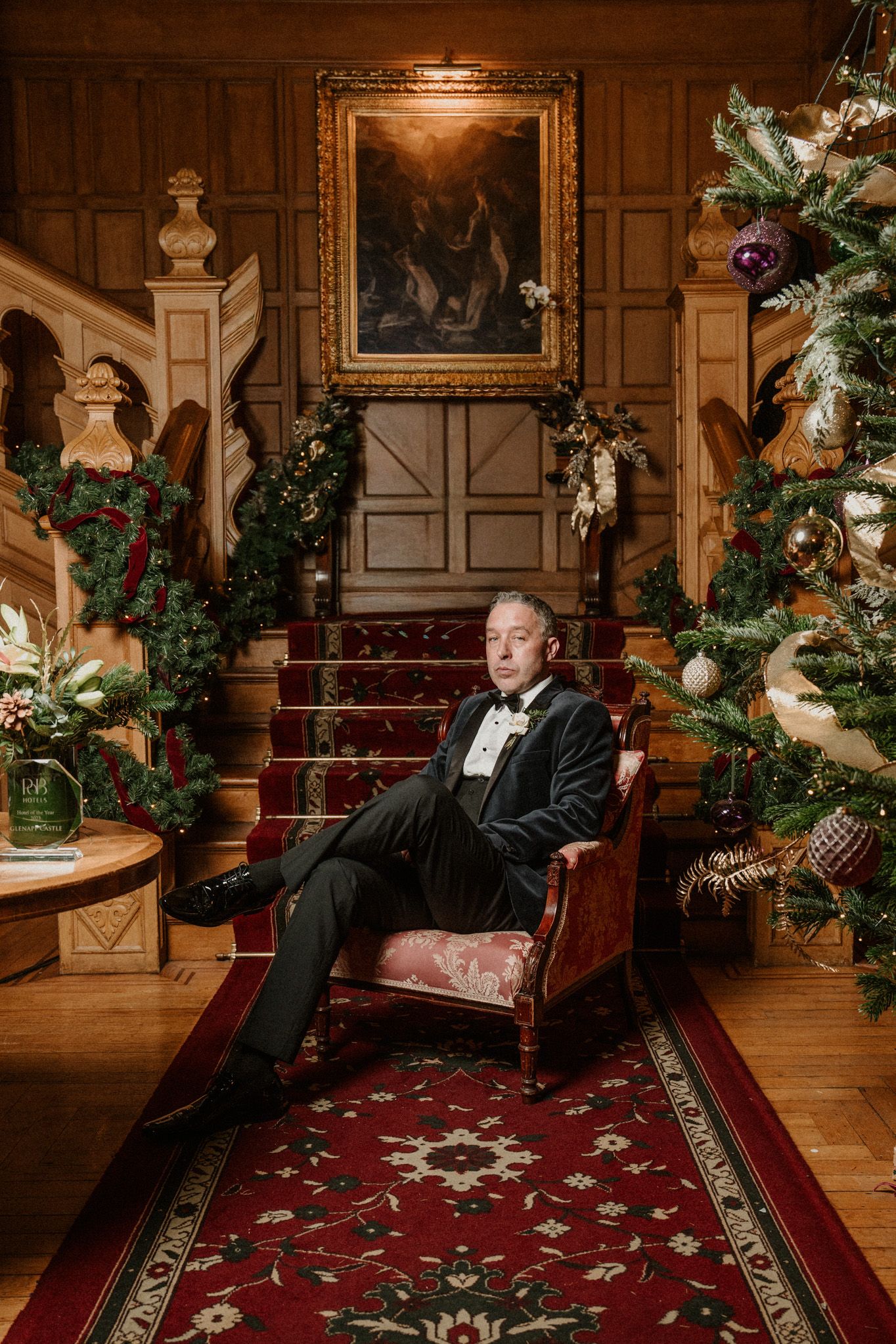 Classic portrait in grand staircase setting with Christmas trees and ornate wood paneling.