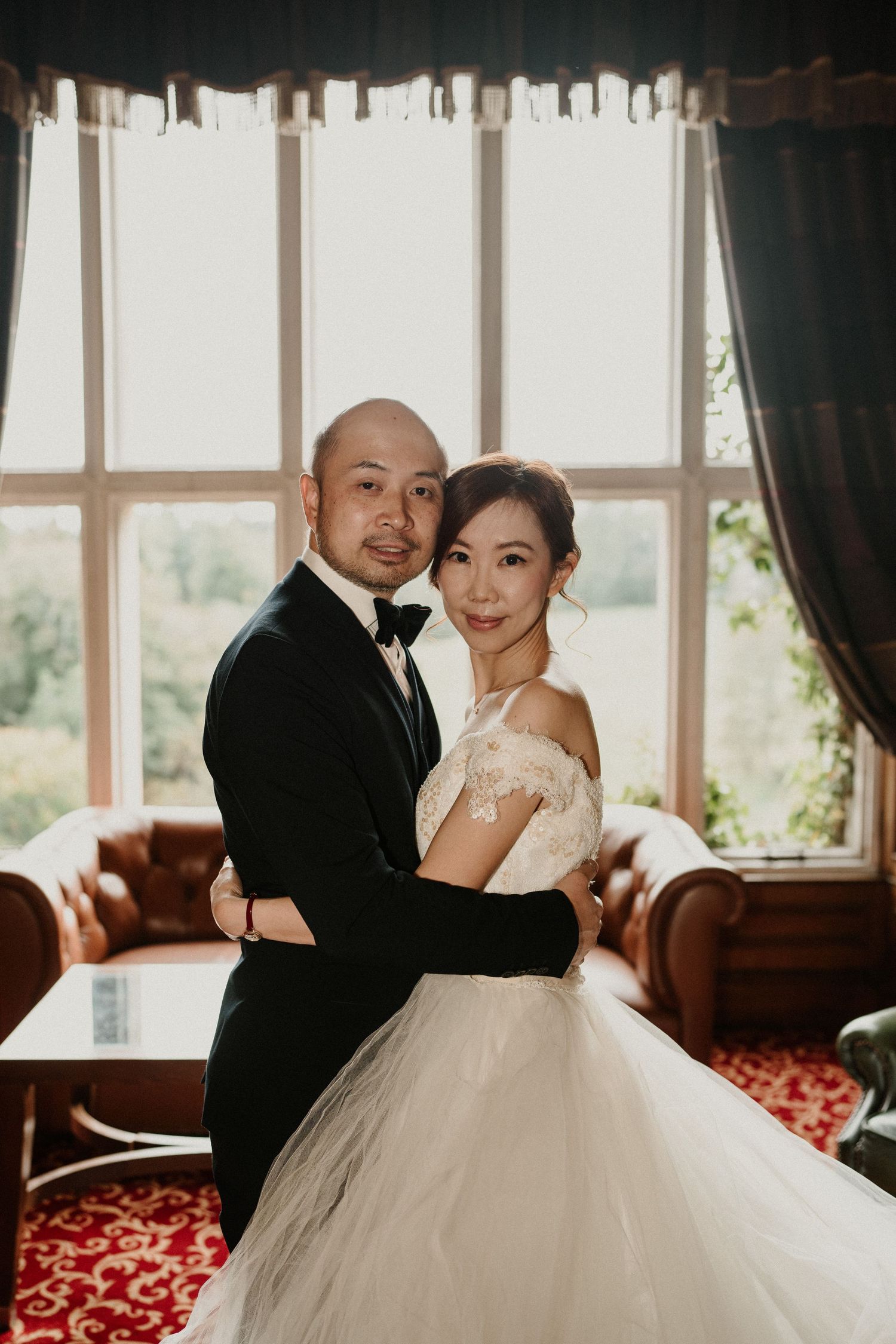 Romantic wedding portrait in an elegant room with large windows and red carpet.