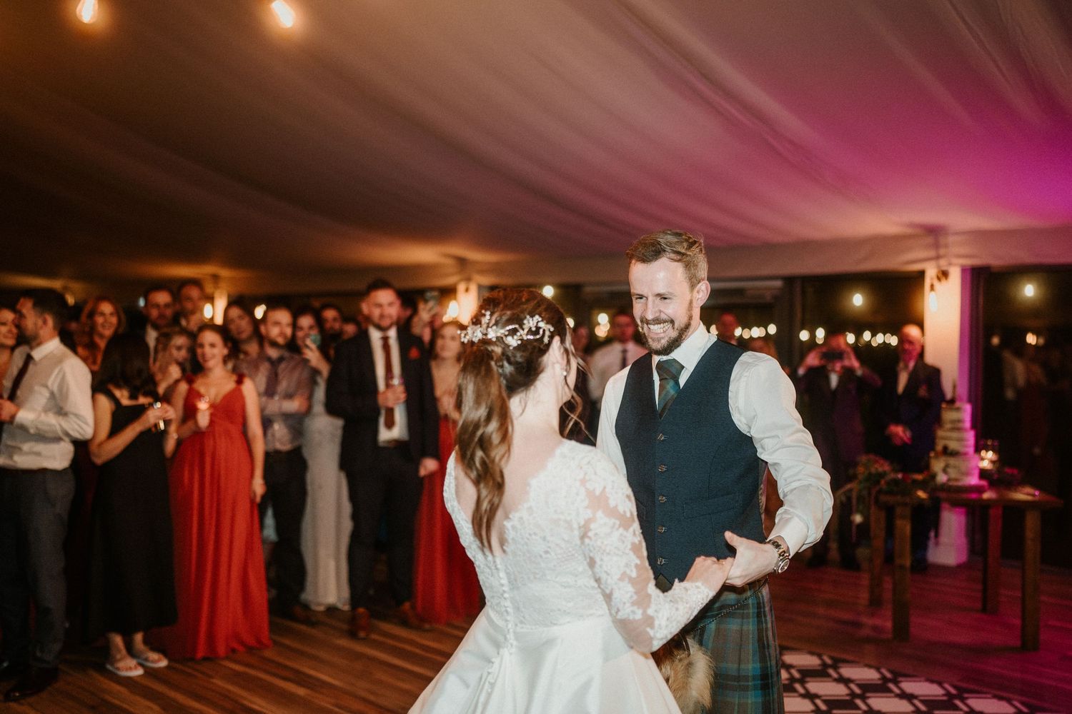 Newlyweds dancing in a tent venue with guests watching from the background.