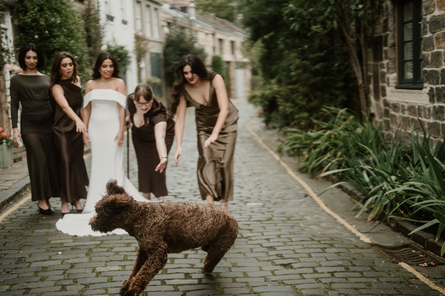 Wedding party poses with vintage car on historic cobblestone street.