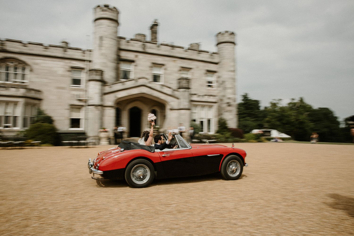 Classic red vintage car parked in front of a grand historic castle building.