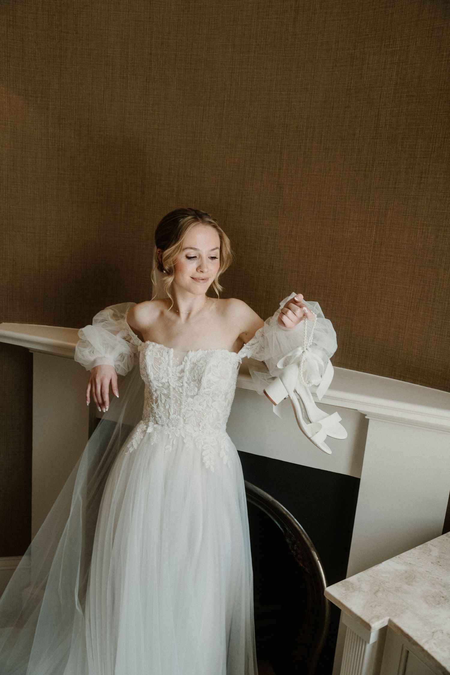 Ethereal wedding gown with off-shoulder neckline and lace details against textured wall.